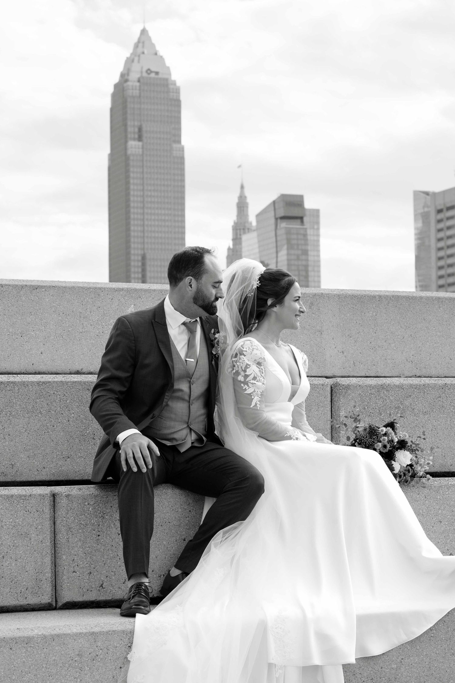 A romantic black and white wedding photo series showing a couple sitting on a rooftop with a city skyline backdrop.