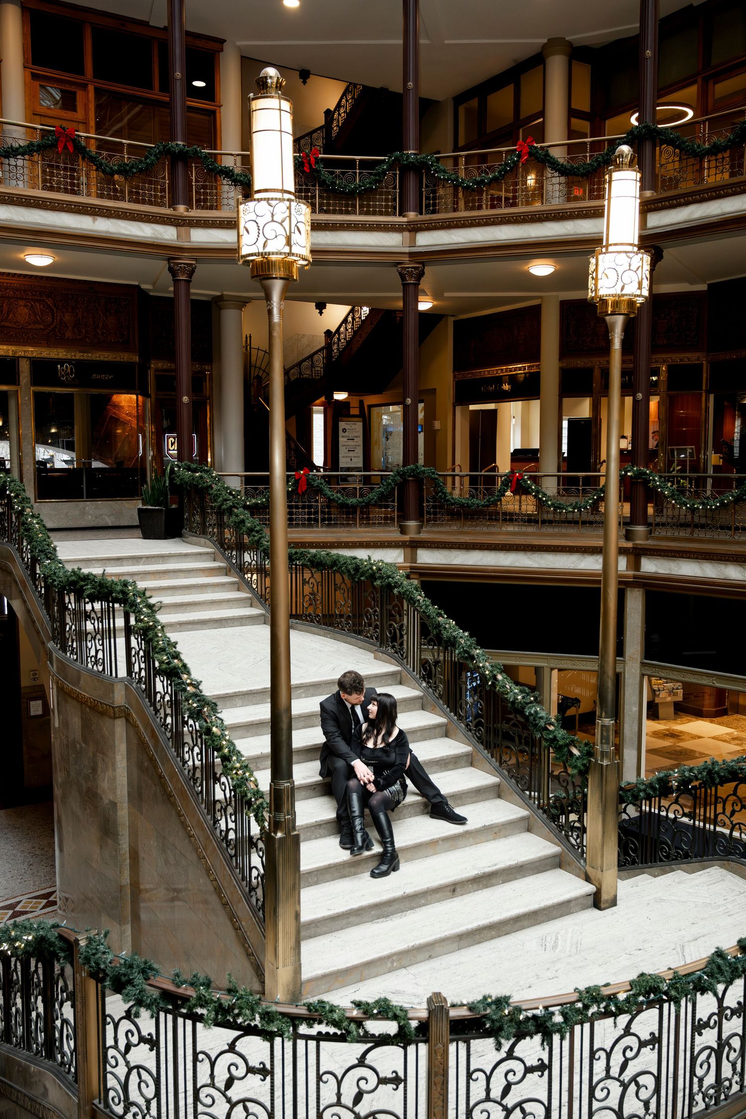 Couple sitting on grand staircase with Christmas garland in elegant multi-level historic building.