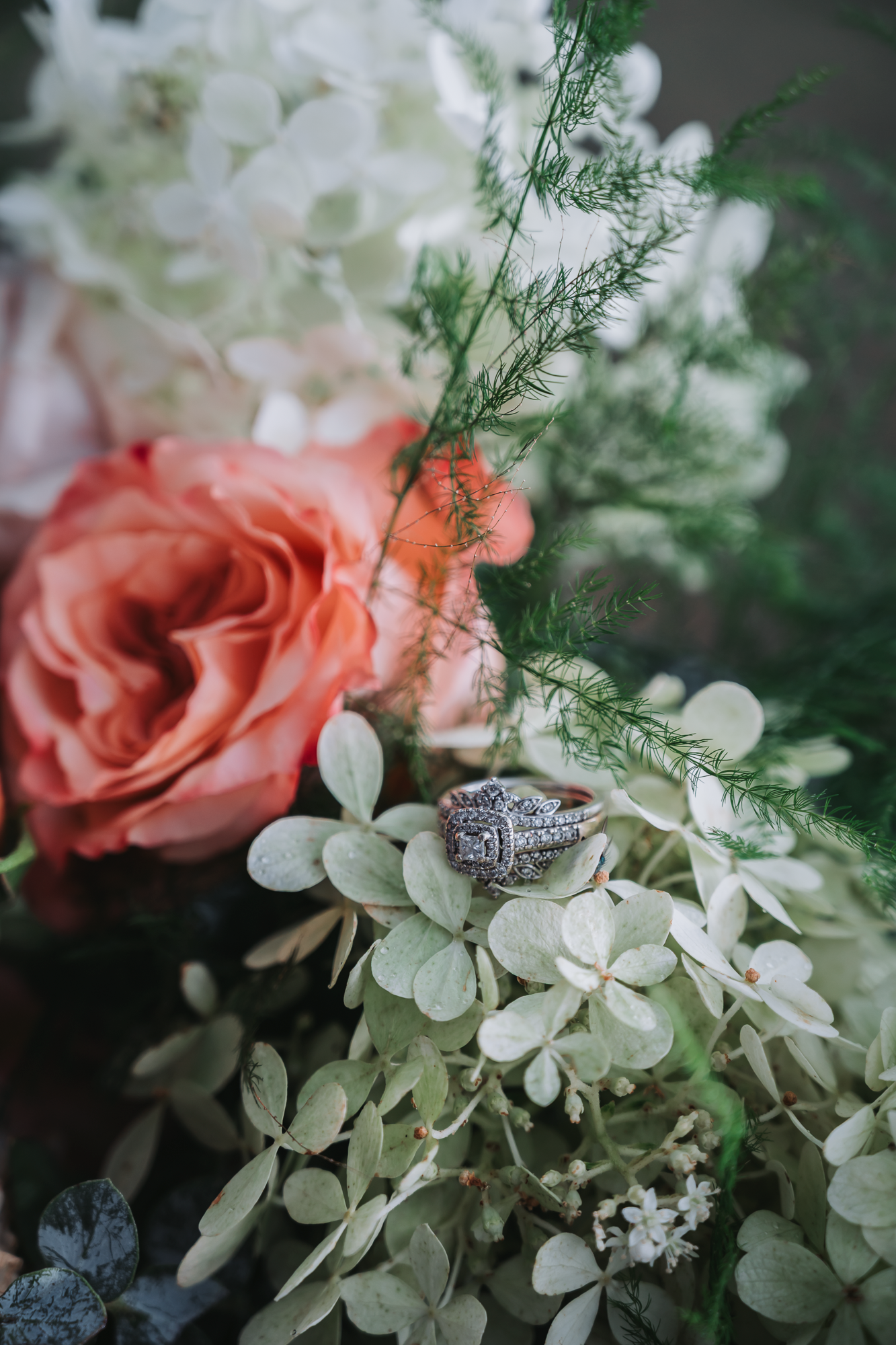 Wedding rings nestled among coral roses and white floral arrangements with delicate greenery.