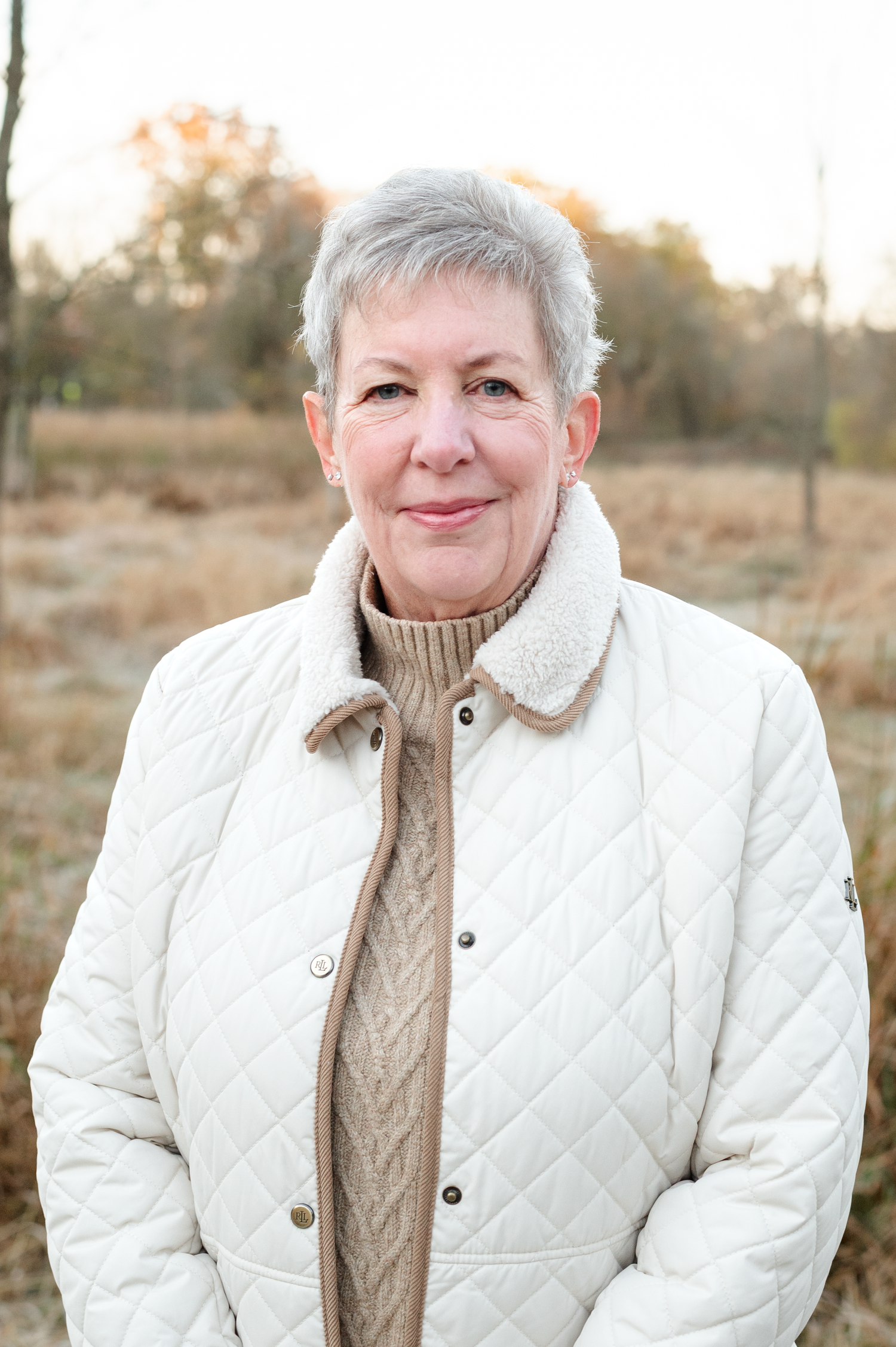 Portrait in warm sunlight wearing a white quilted jacket and beige sweater.