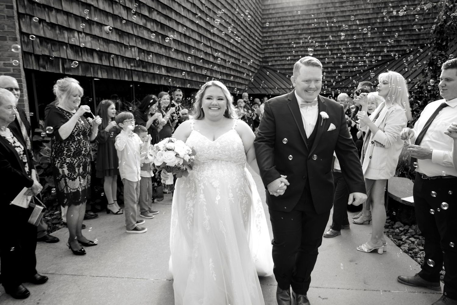 A black and white wedding reception photo showing guests dancing and celebrating on a dance floor.