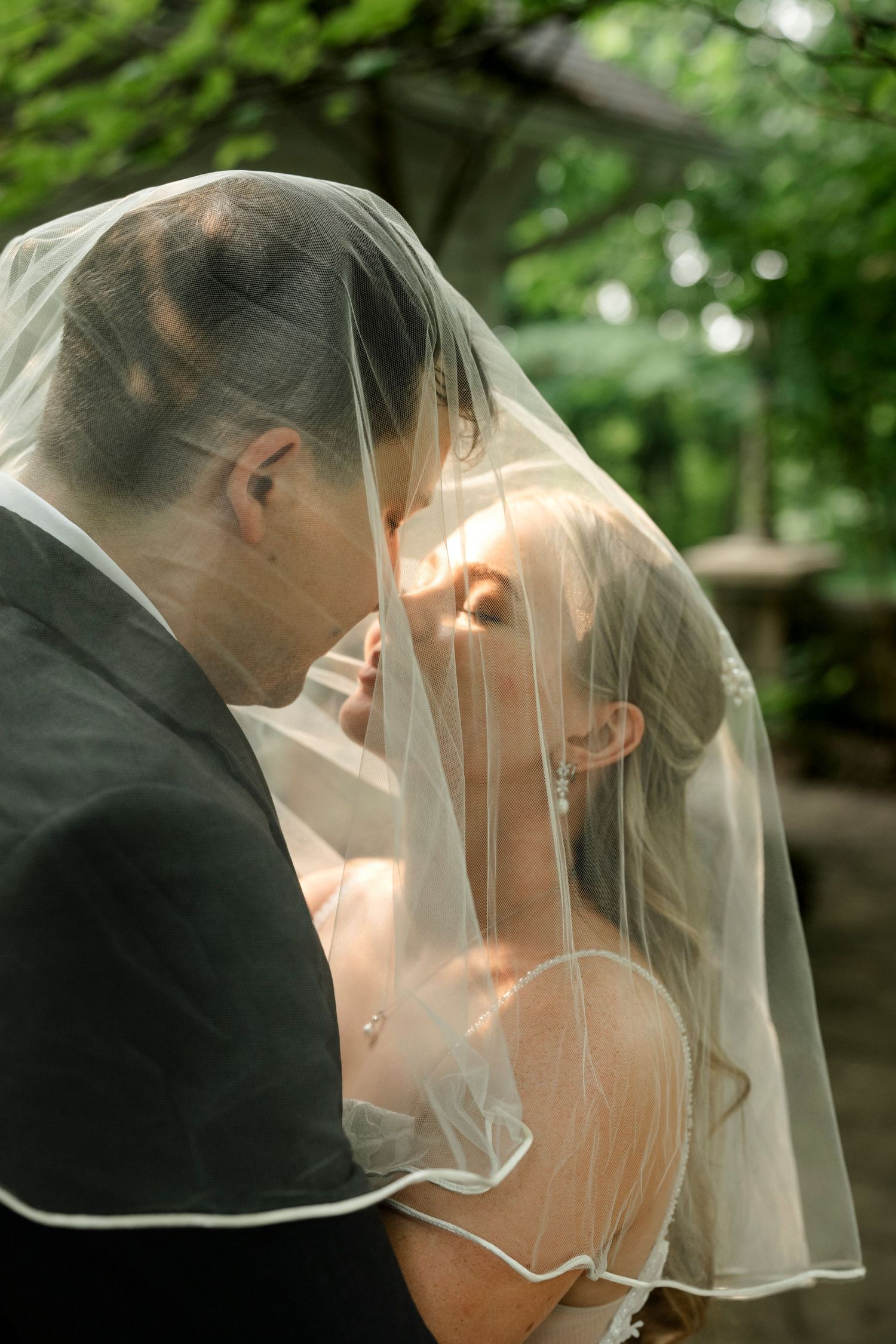 Bride and groom sharing a romantic kiss under a flowing wedding veil outdoors.