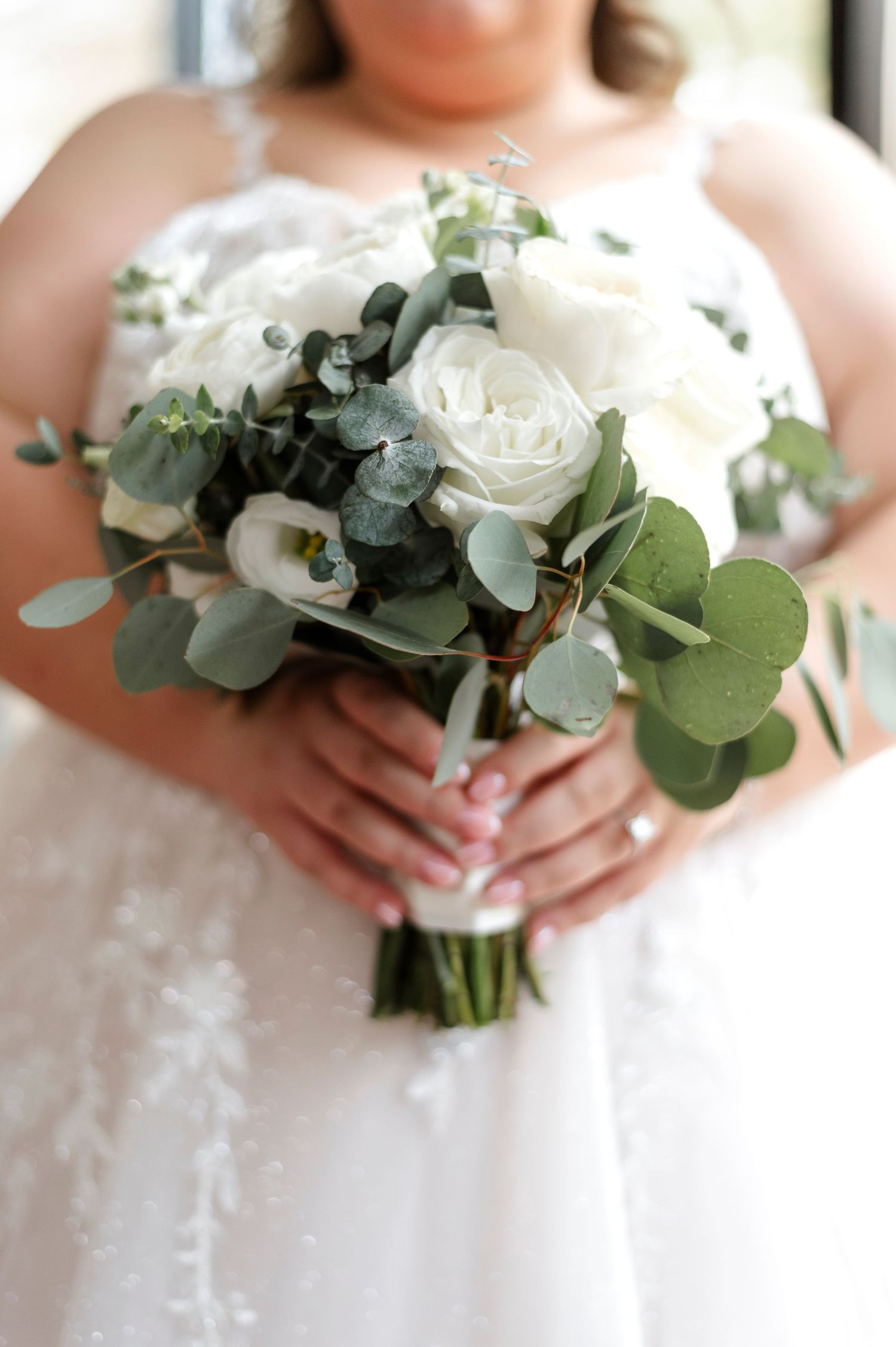White roses and eucalyptus leaves create elegant wedding bouquets held against a lace dress.
