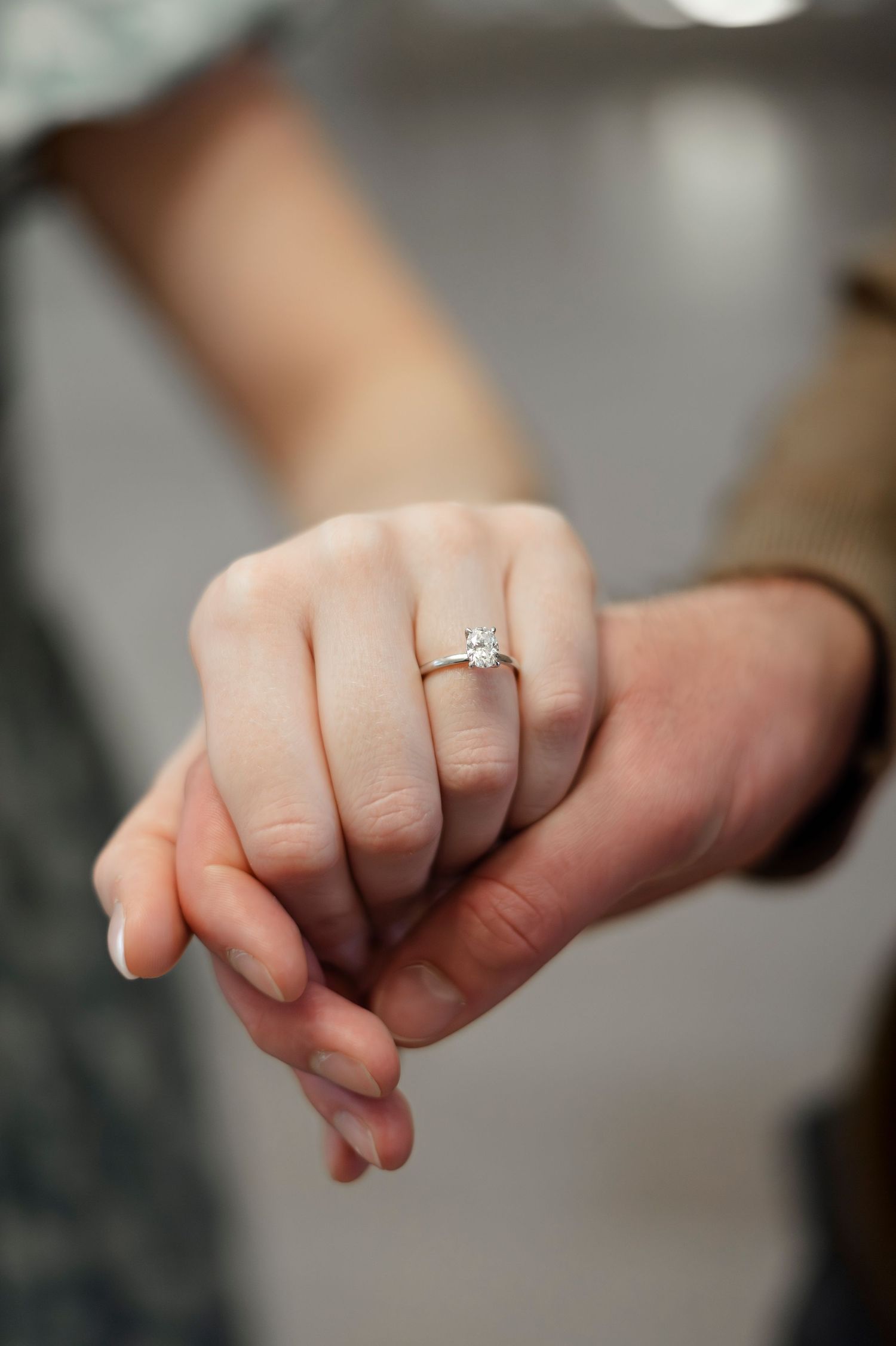 Close-up of a woman's hand wearing a solitaire diamond engagement ring while holding hands with her partner.