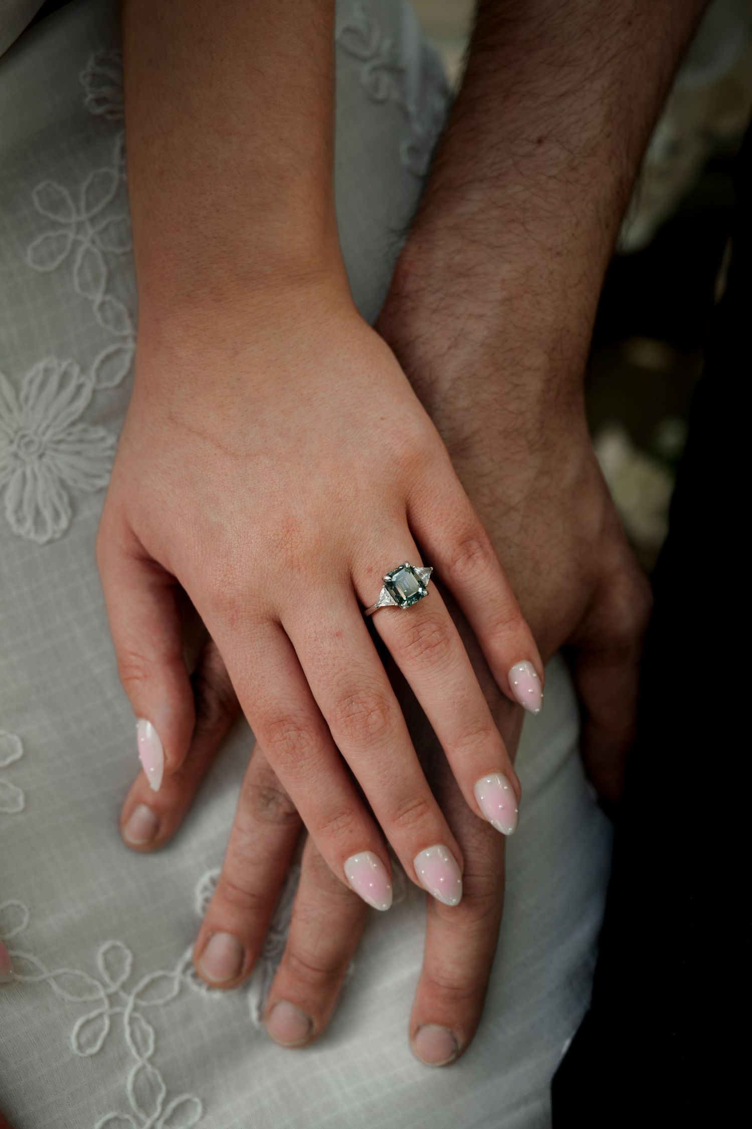 Close-up of hands showing an elegant emerald-cut engagement ring with side stones on manicured fingers.