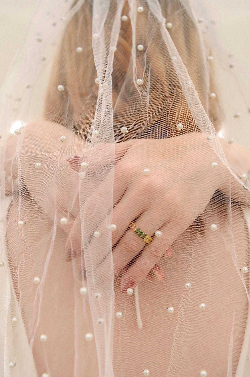 Close-up of hands wearing a ring under a delicate pearl-studded veil.