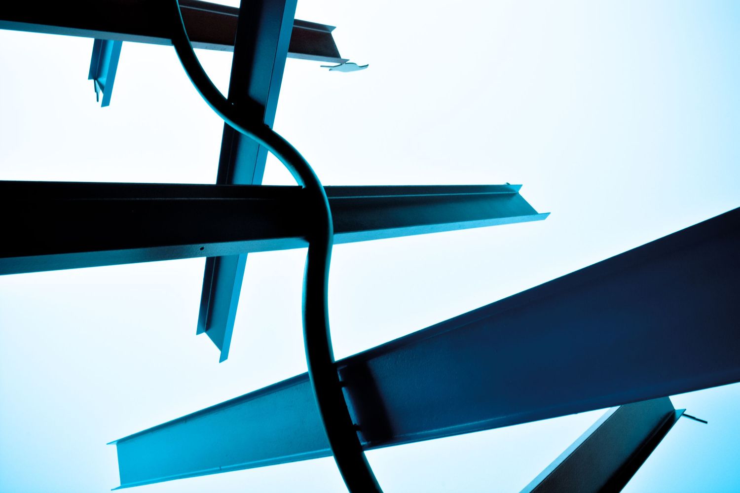 Abstract architectural detail of intersecting steel beams against bright sky in blue tones.