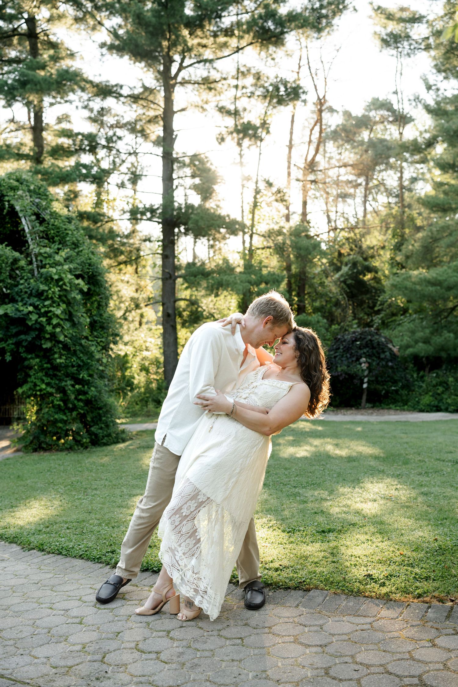 Couple sharing a romantic dip kiss in a lush garden setting, bride in white lace gown and groom in beige suit.