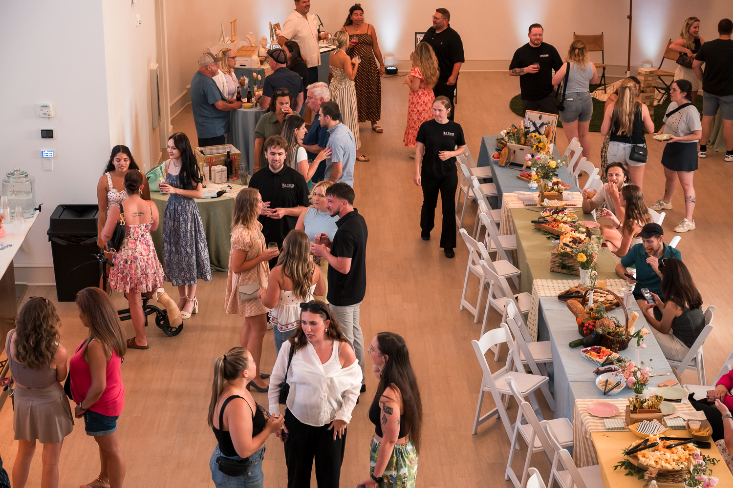 People gather around buffet tables at a social event in a large room with peach-colored walls.
