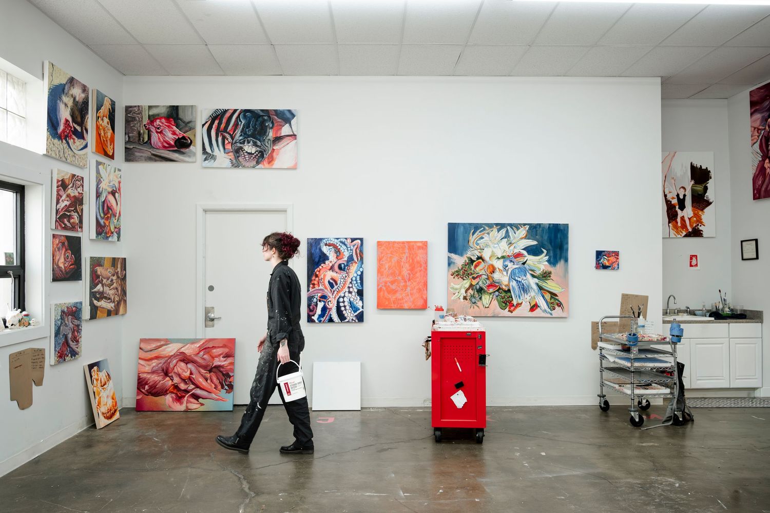 Long white gallery space with artwork displayed on walls and figures walking through viewing the exhibition.