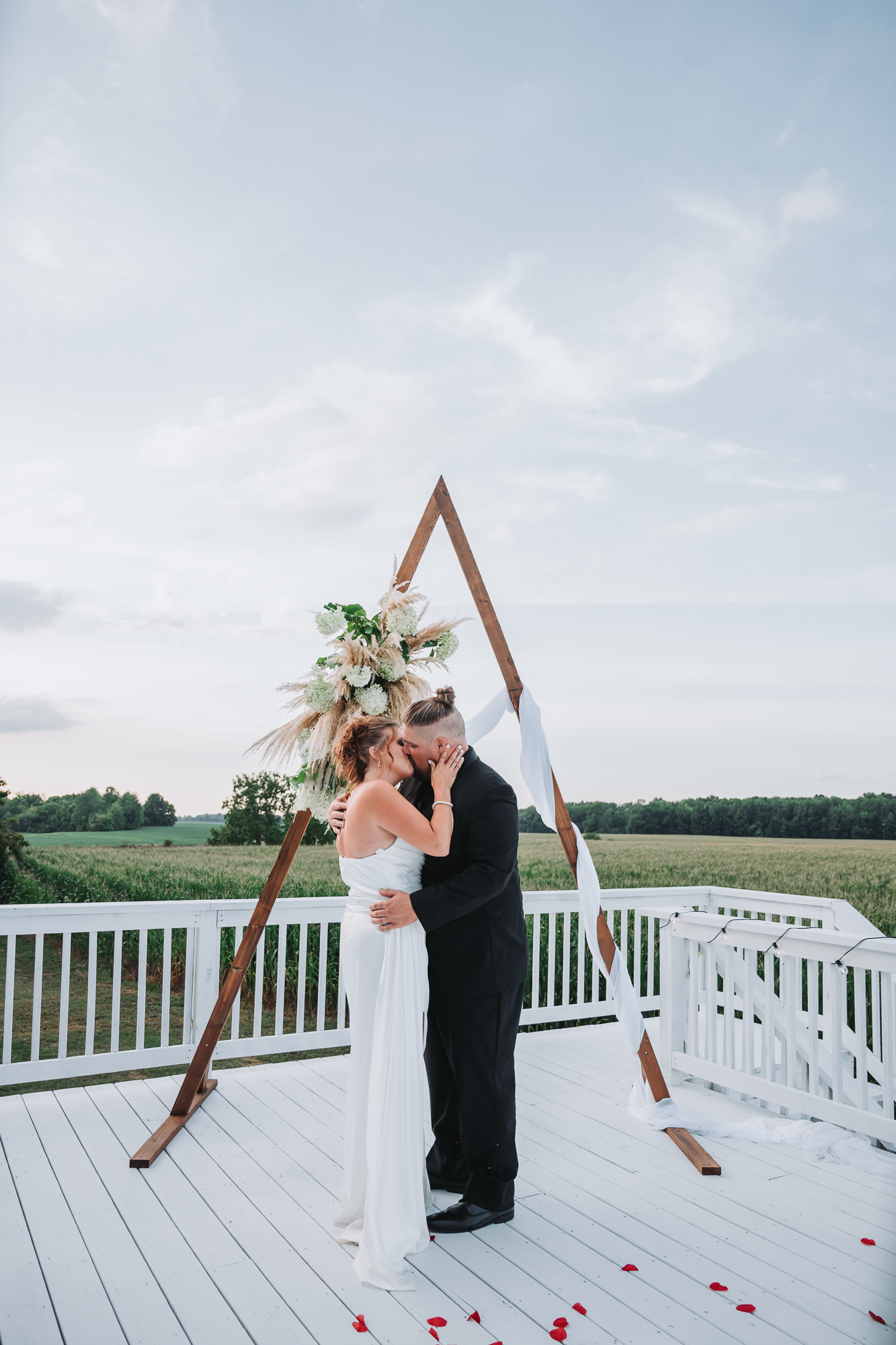 Wedding ceremony setup on a white deck overlooking scenic countryside with wooden arch.