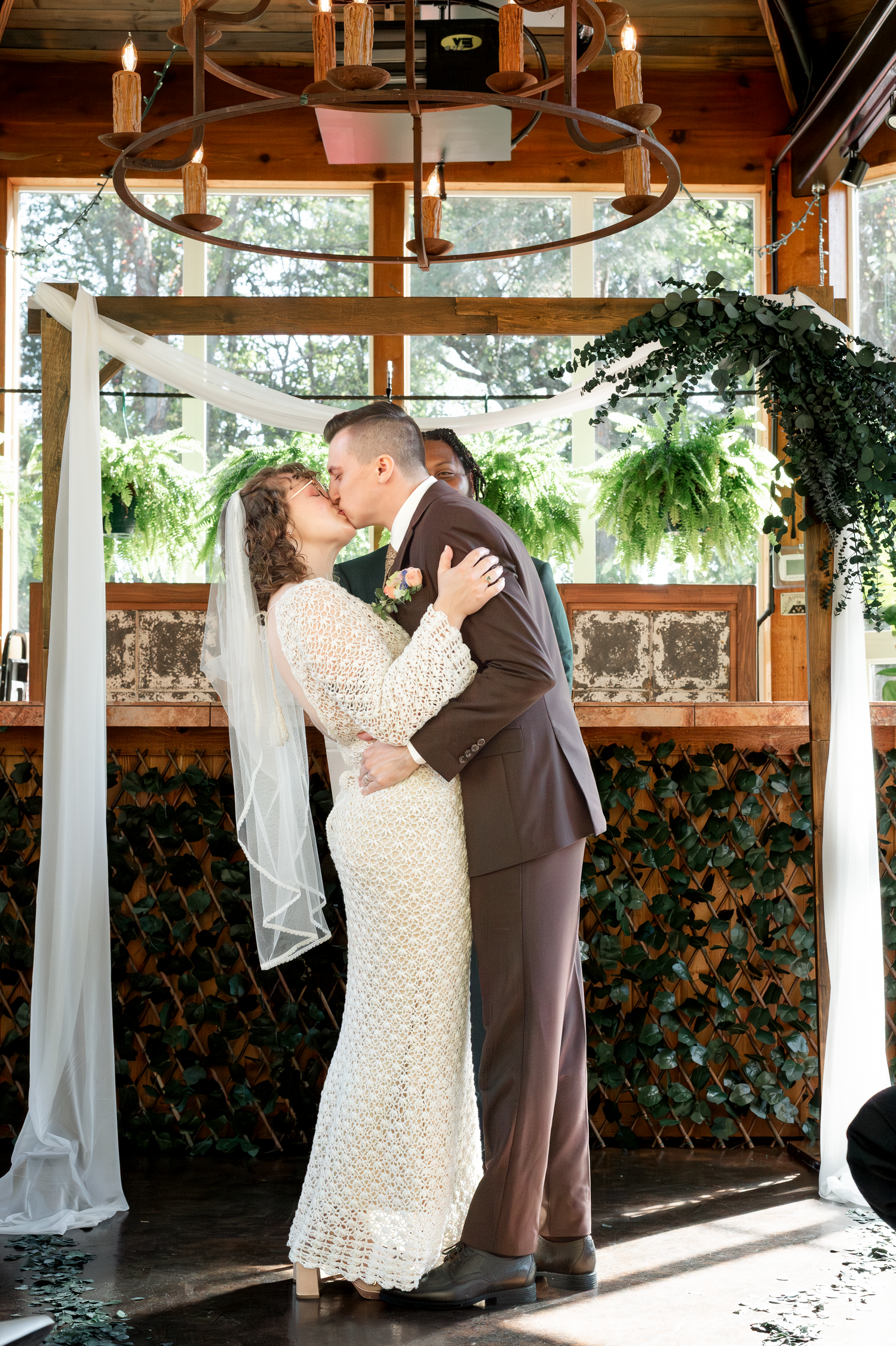 Wedding ceremony in a rustic pavilion decorated with white drapes and greenery.