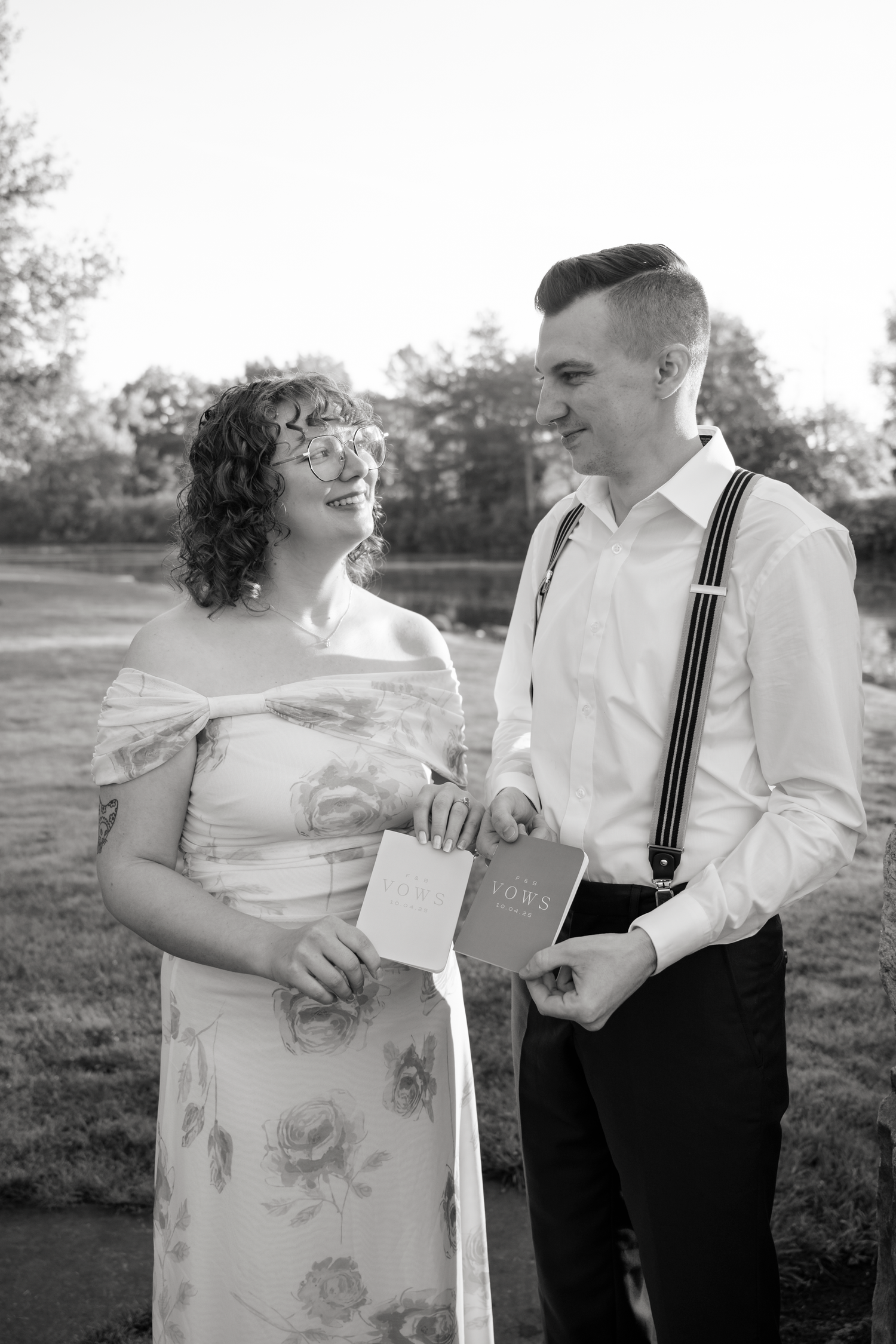 A romantic couple in vintage-inspired attire share a sweet moment together in a grassy outdoor setting at sunset.
