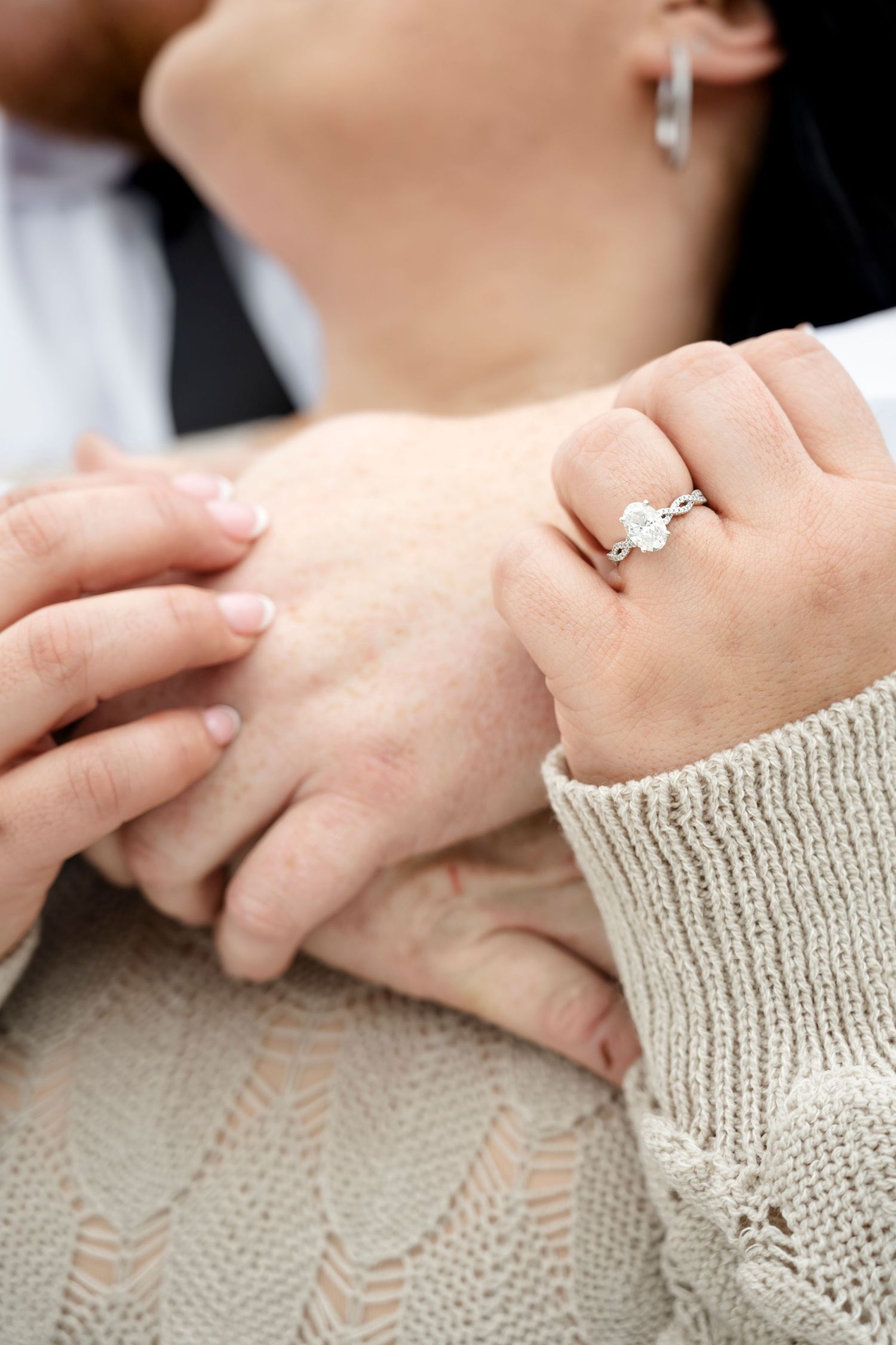 Close-up of a woman's hand wearing a diamond engagement ring while holding hands with her partner.