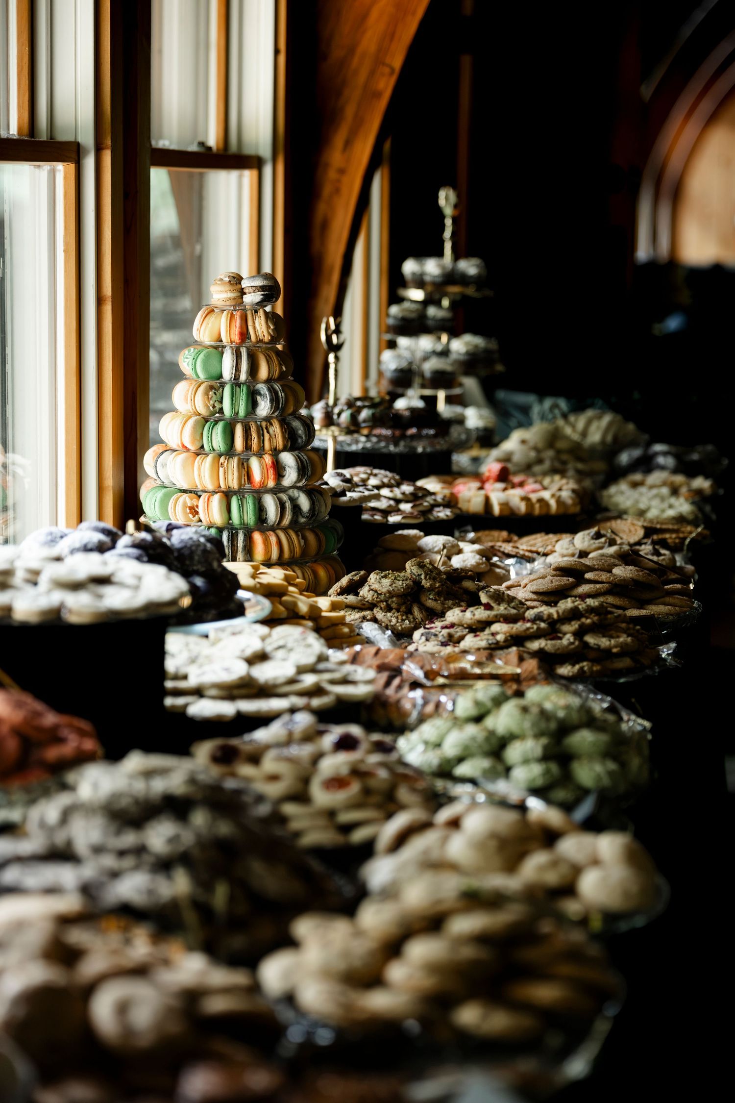 Elegant dessert table with macaroon tower, cookies, and pastries displayed near arched windows at an event.