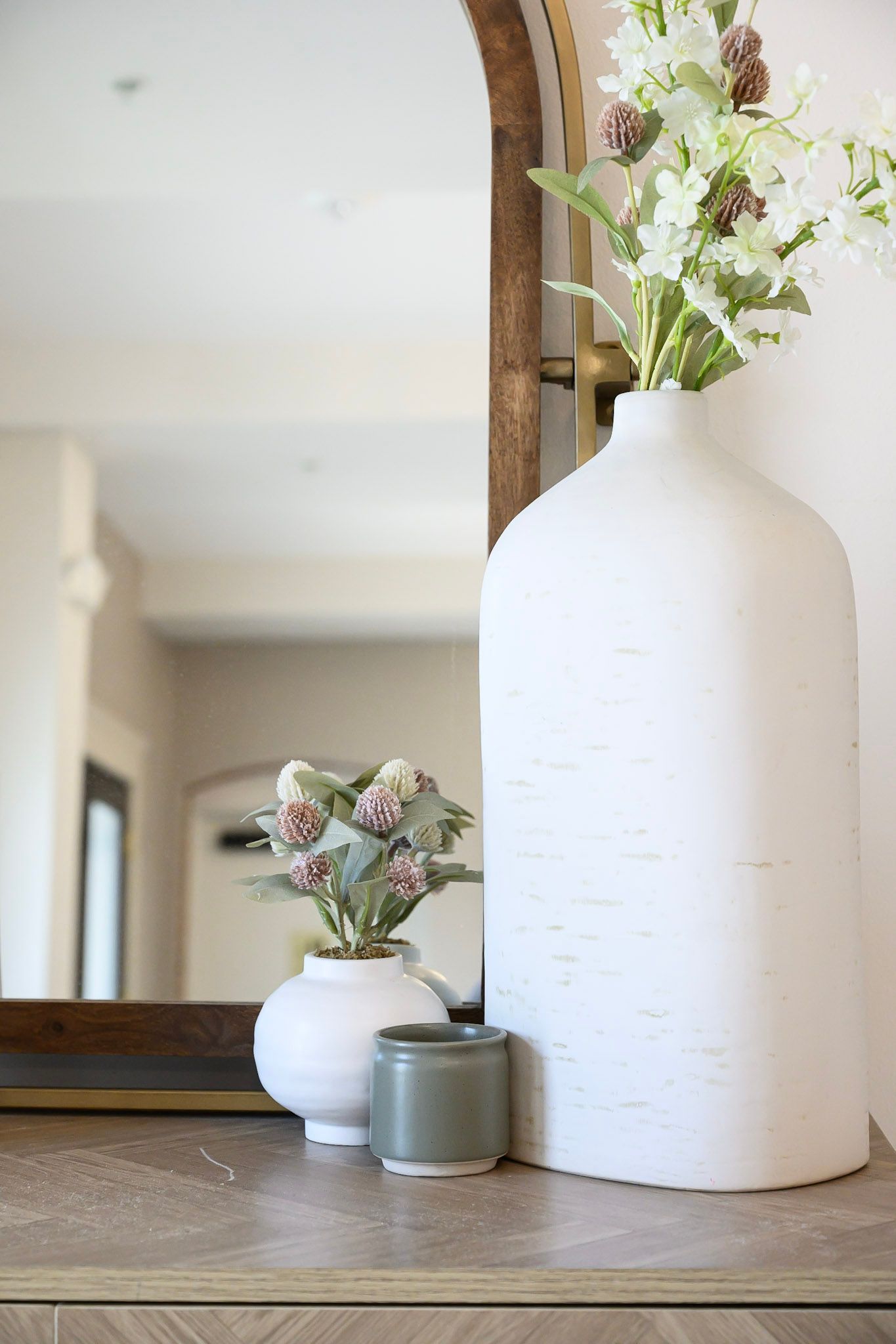 White ceramic vases and potted plants arranged on wooden table with mirror in modern farmhouse style decor.