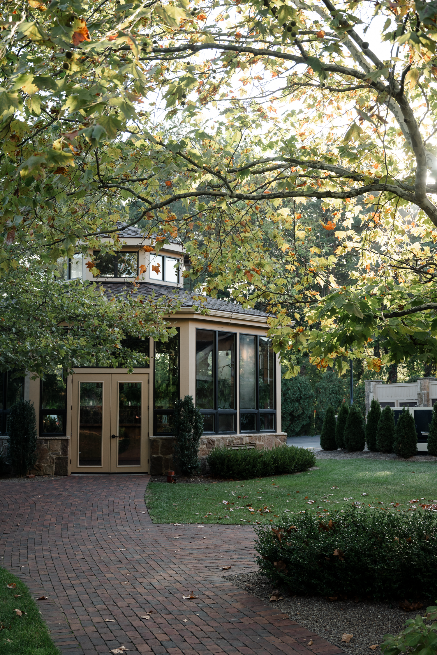 Modern ranch-style home with brick patio and large windows surrounded by autumn trees and manicured landscaping.