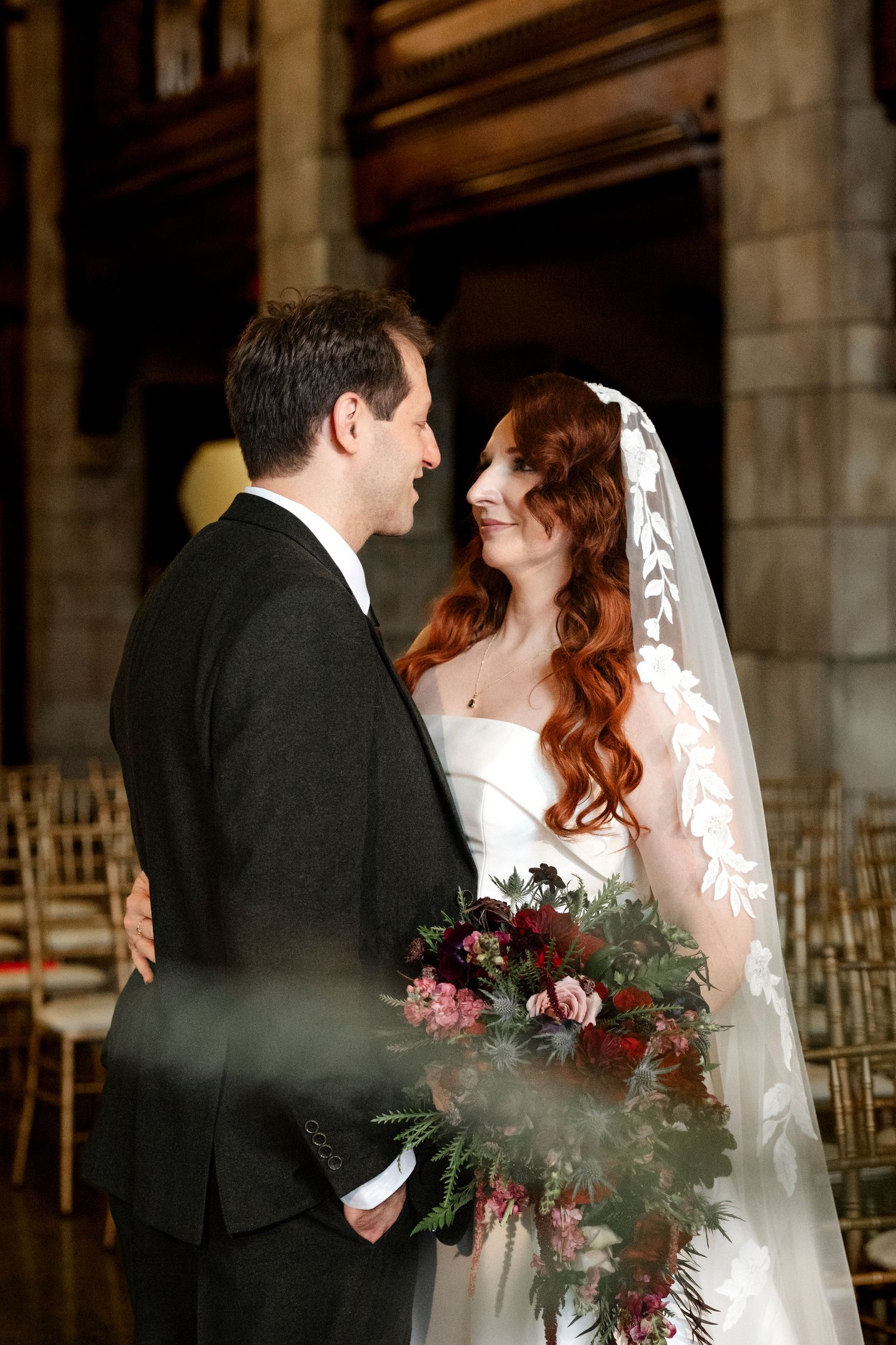 Romantic wedding couple shares intimate moments in a rustic venue with dark wood beams and elegant chairs.