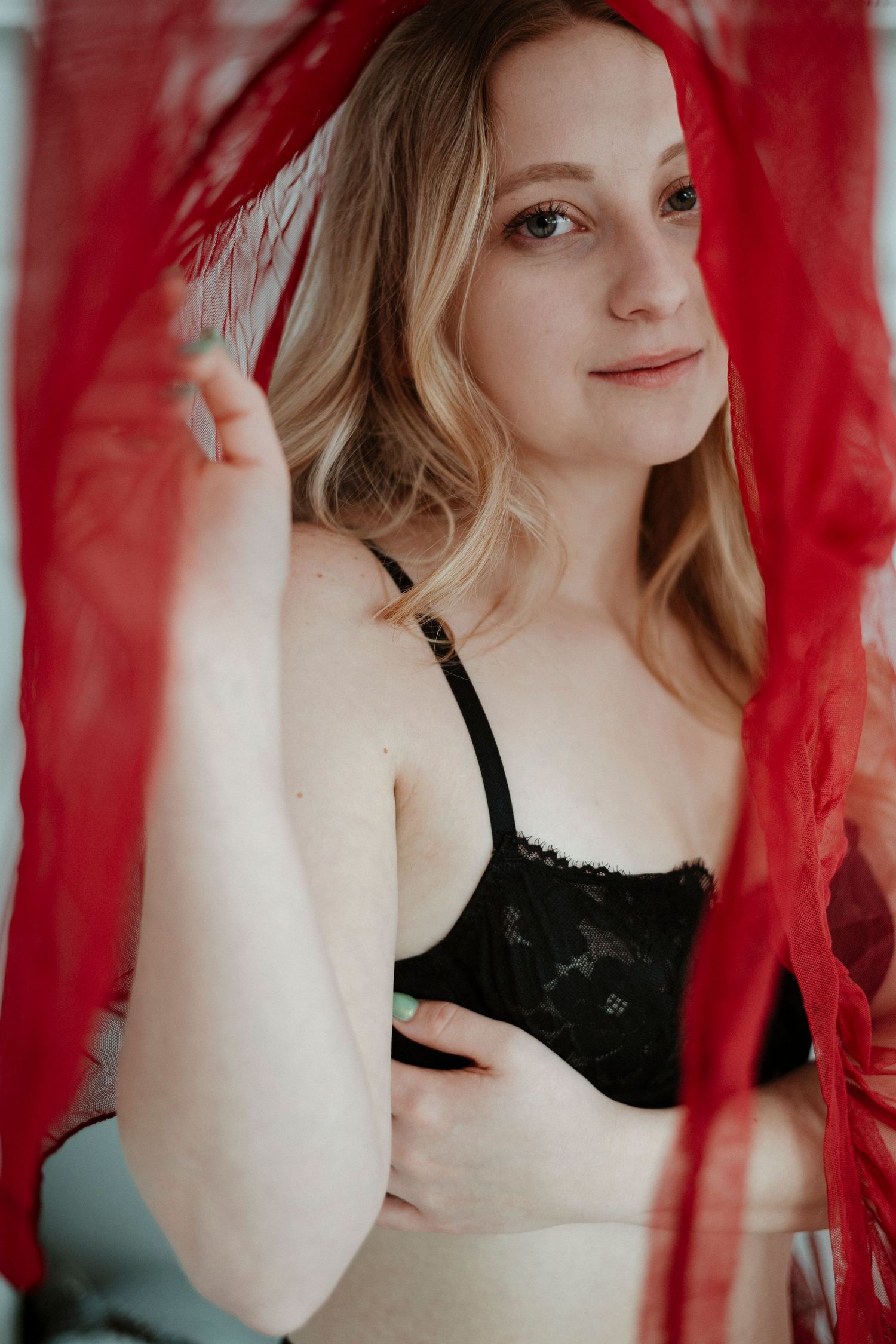 Artistic portrait through sheer red fabric showing a dreamy ethereal mood in black attire.