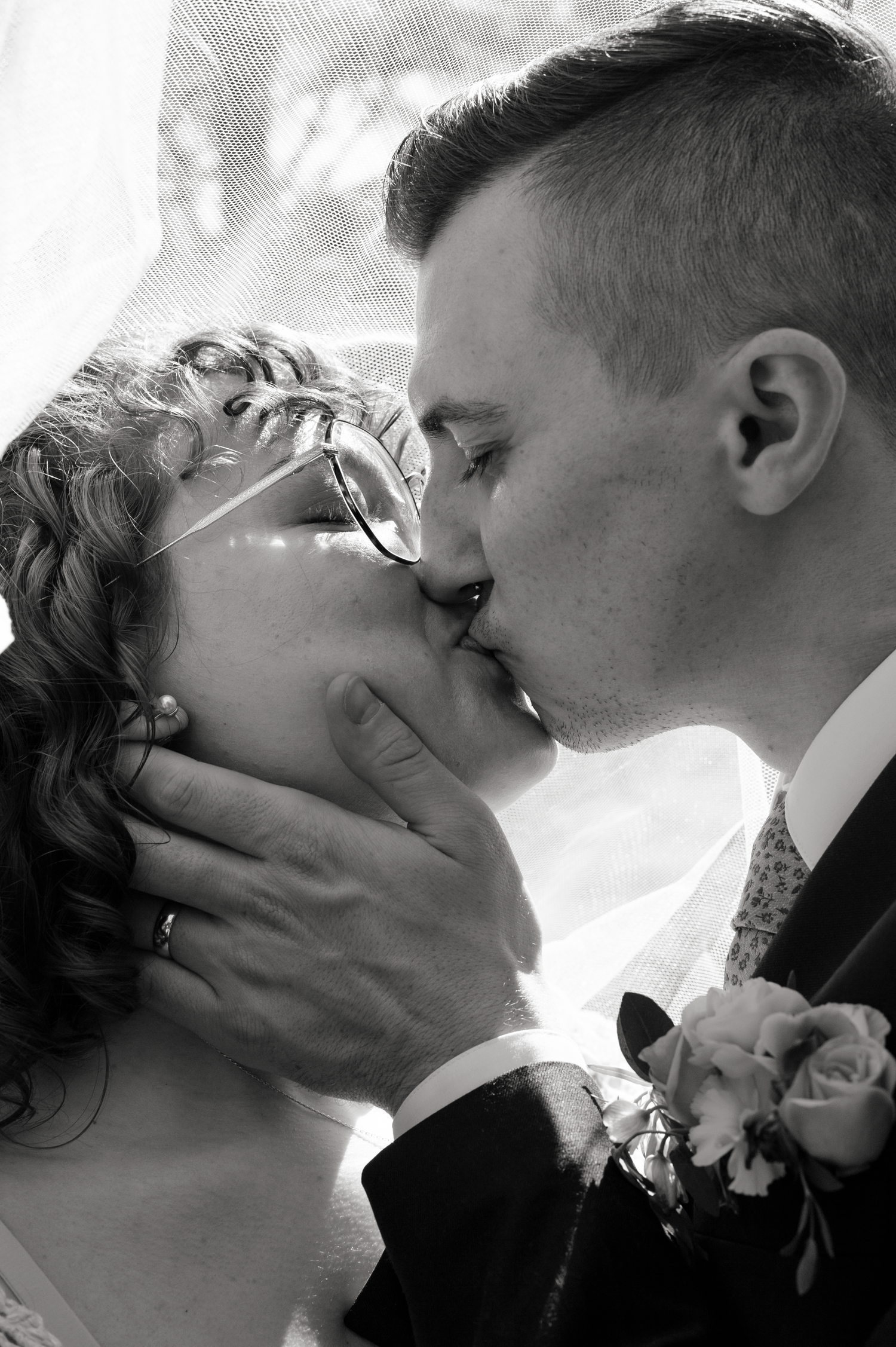 A romantic black and white wedding photograph captures a tender kiss between newlyweds wearing formal attire.