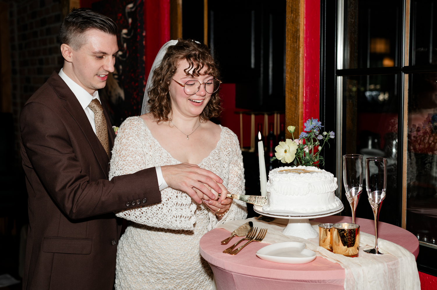 A couple in wedding attire cuts their white wedding cake together at an elegant reception venue.