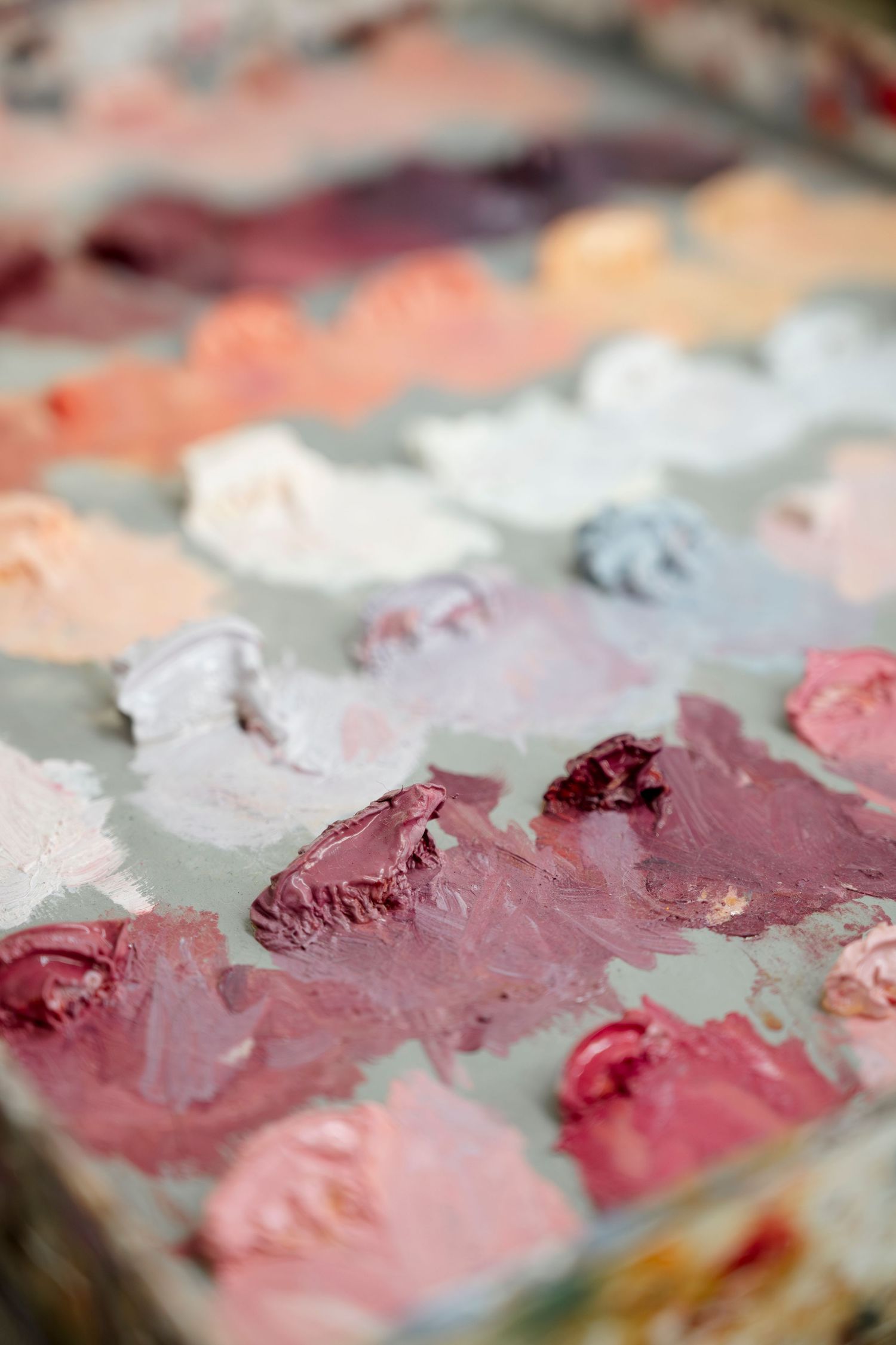 Close-up of pink and burgundy oil paint palette showing rich textural mixing of colors.