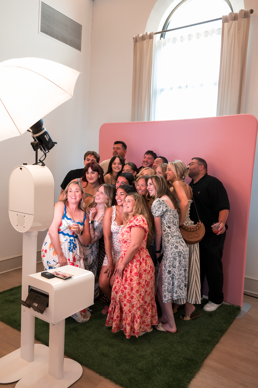 Group of guests gathered in front of a pink backdrop at a photo booth during an indoor event.