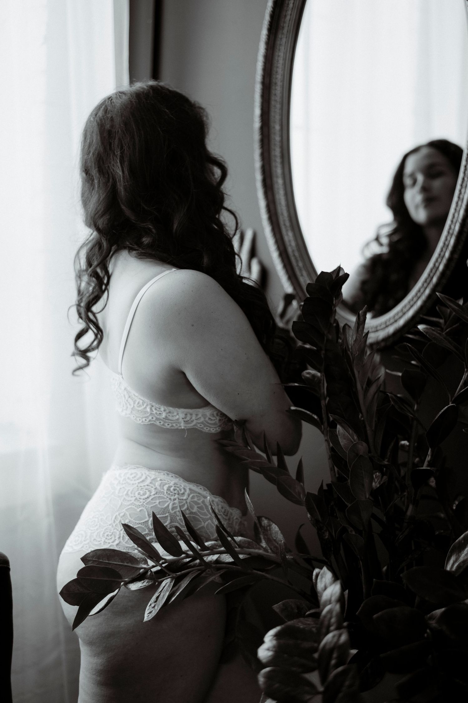 Black and white boudoir photo series showing a woman in lingerie posing near a window in soft natural light.