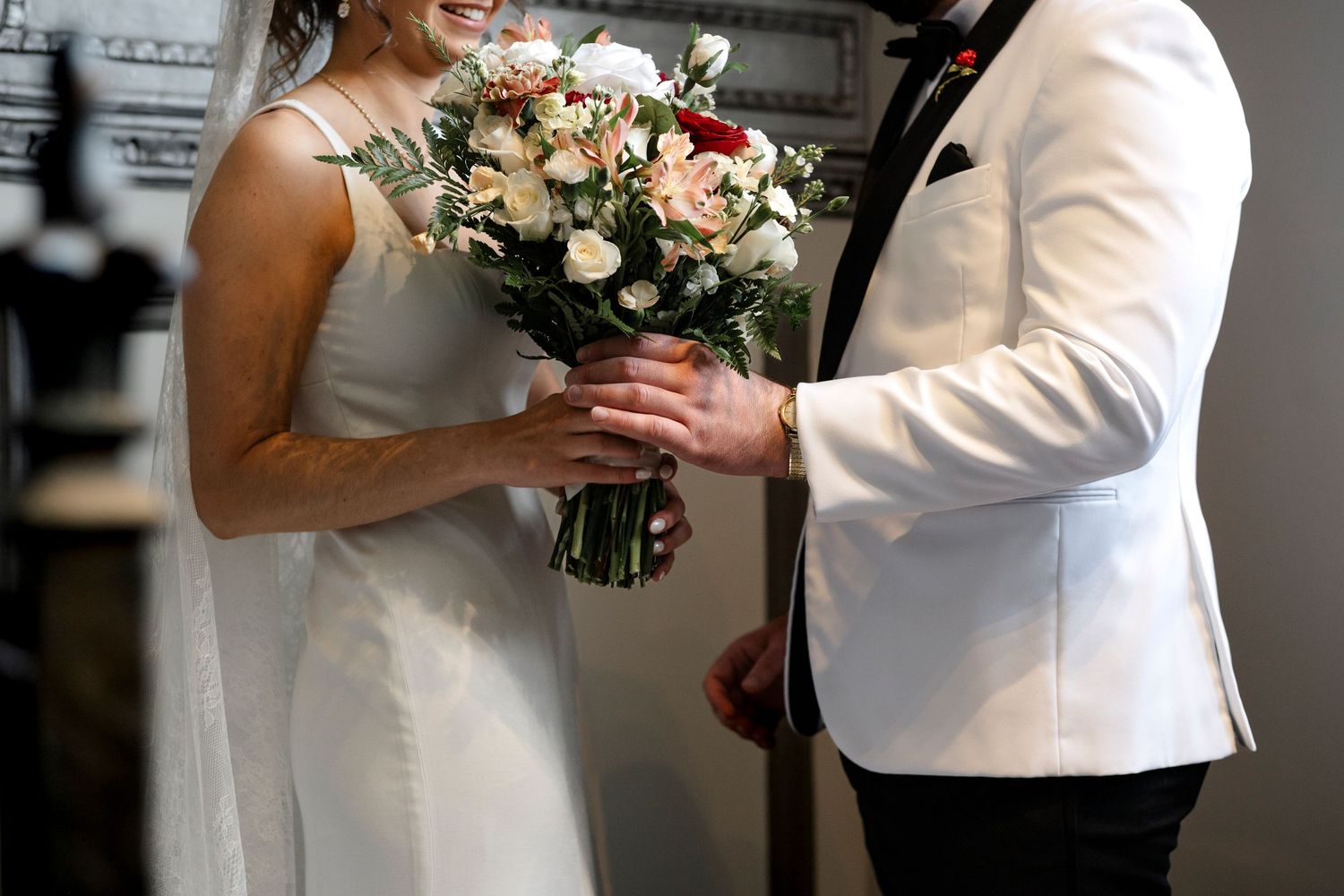 A bride and groom embrace and hold a bouquet of flowers on their wedding day.