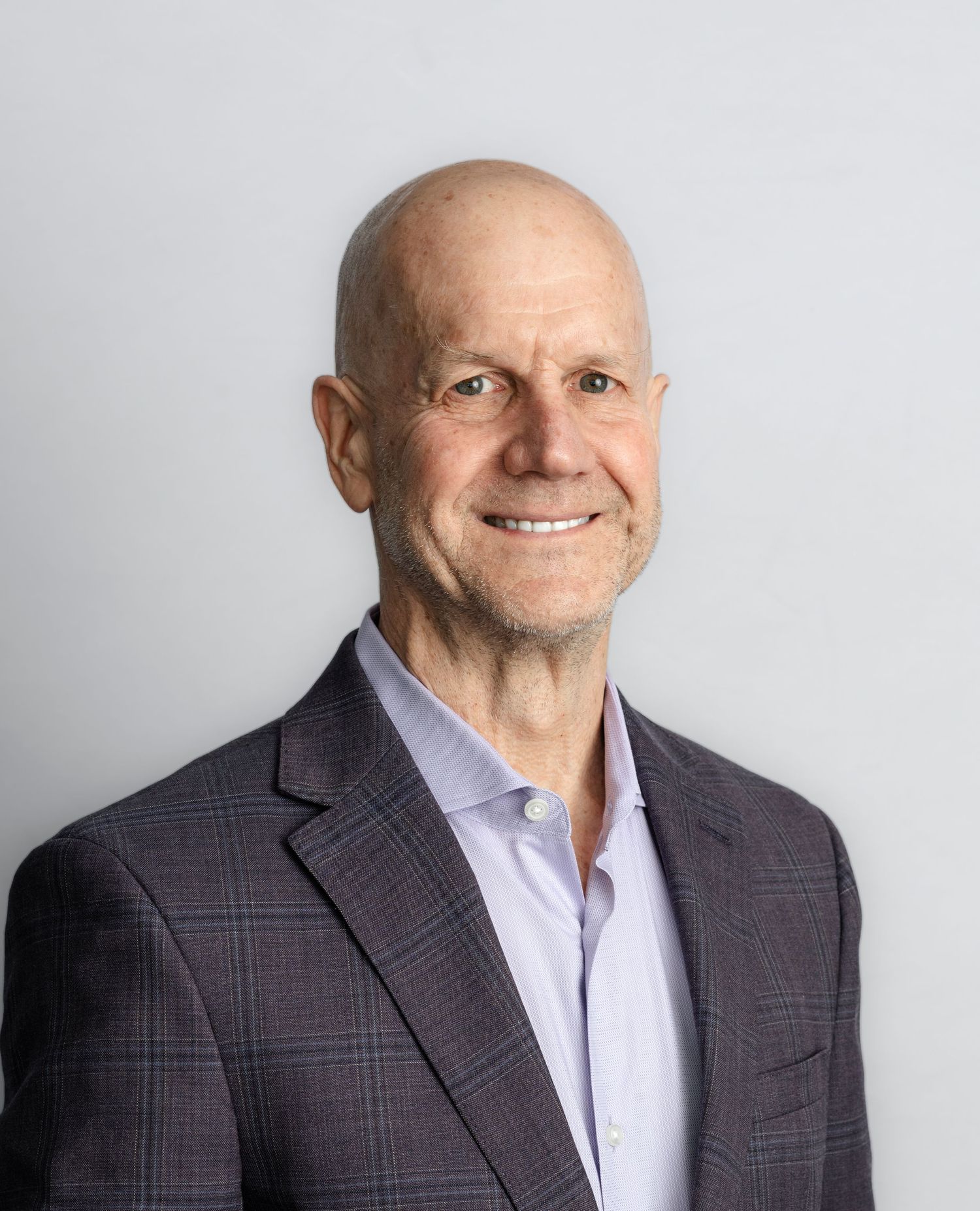 Professional headshots of a bald person in a plaid suit jacket and light shirt against a white background.