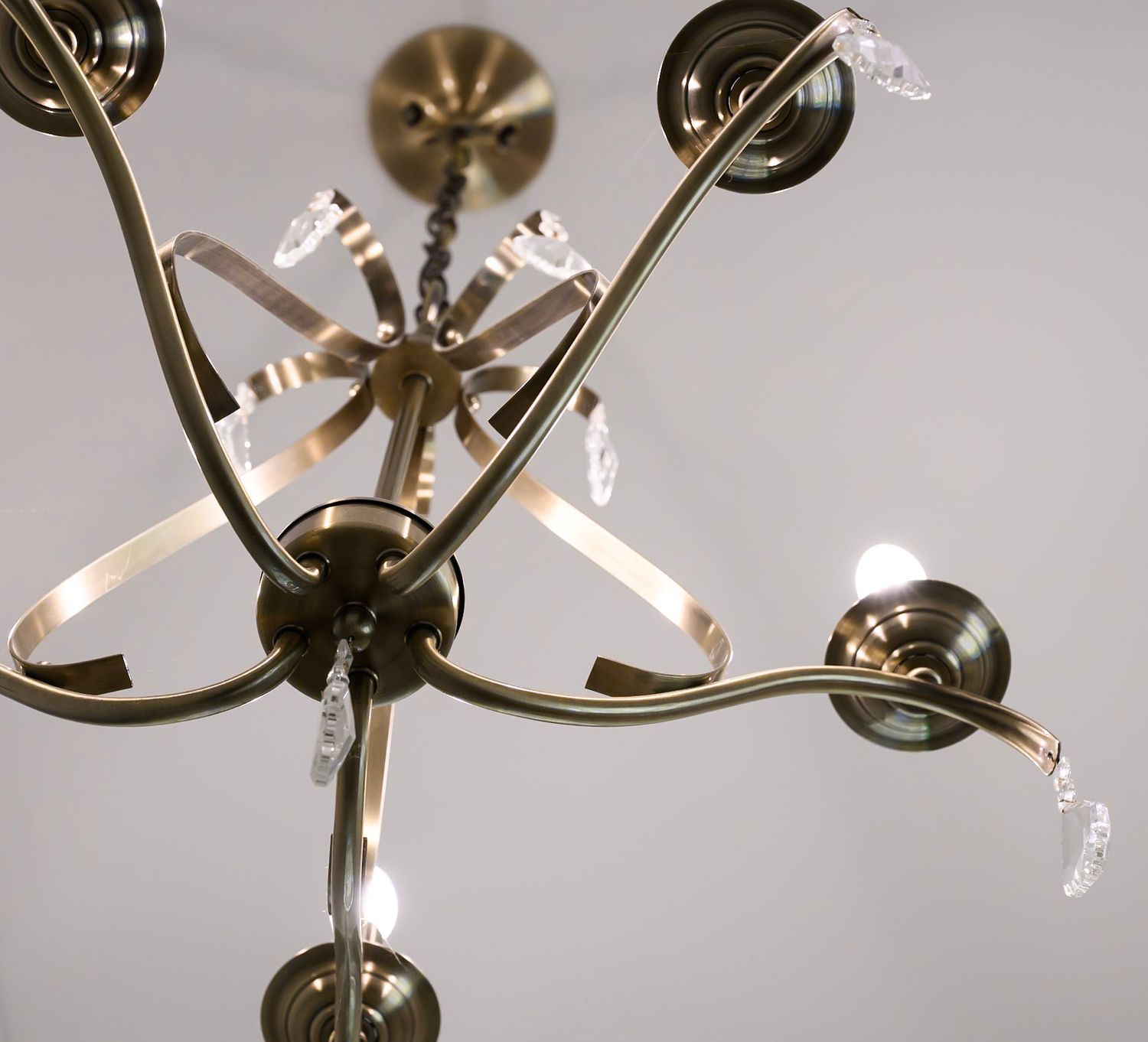 Modern brass chandelier with multiple curved arms and light fixtures hangs elegantly against a gray background.