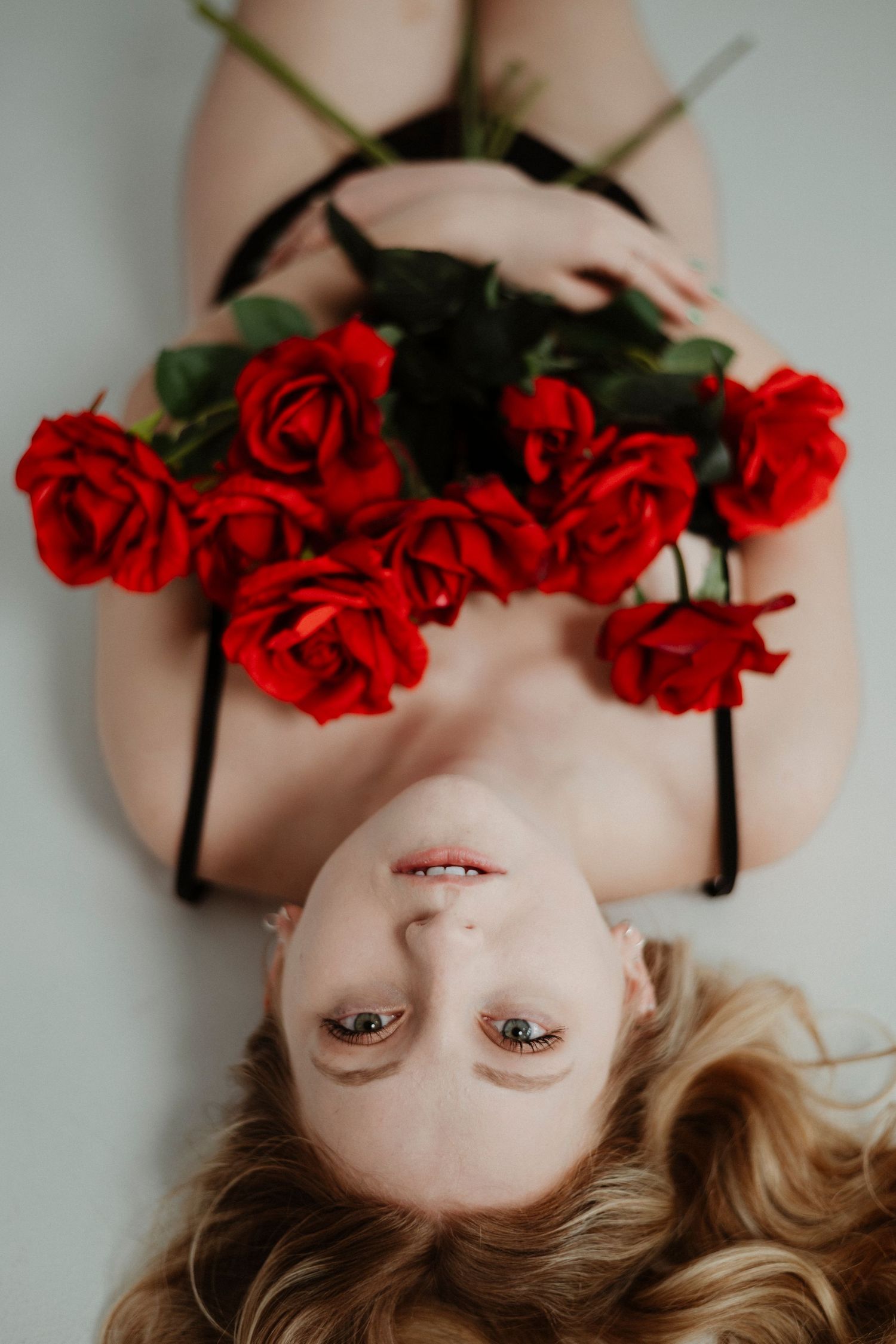 A person wearing a crown of red roses lies against a light background in a series of artistic portrait poses.