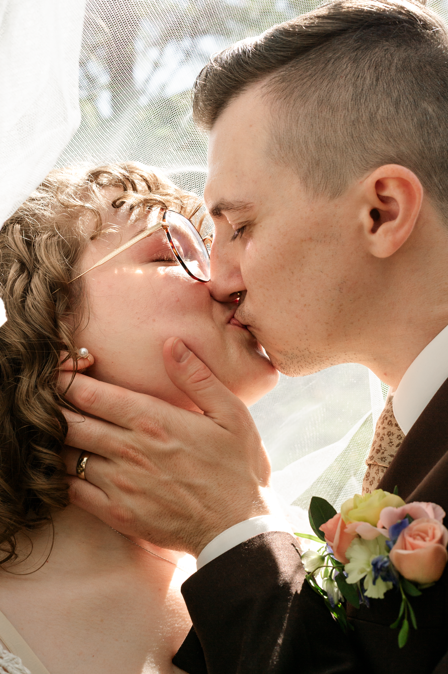 Intimate wedding kiss captured in soft natural light with floral boutonniere.