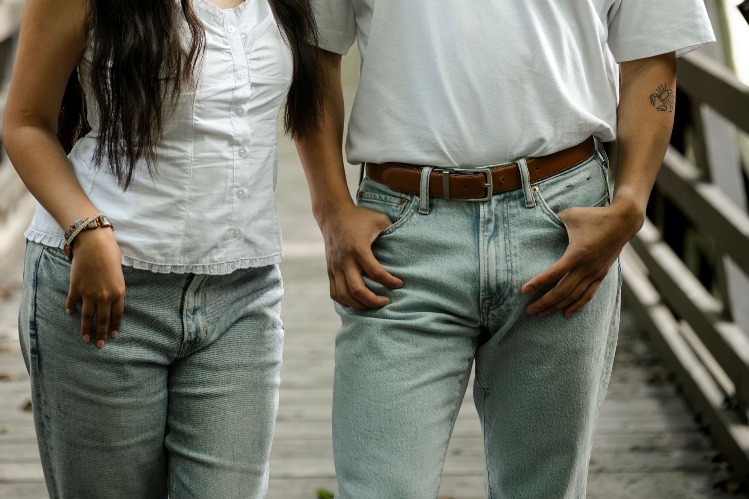 Two people wearing white shirts and light blue jeans standing side by side on a wooden bridge.