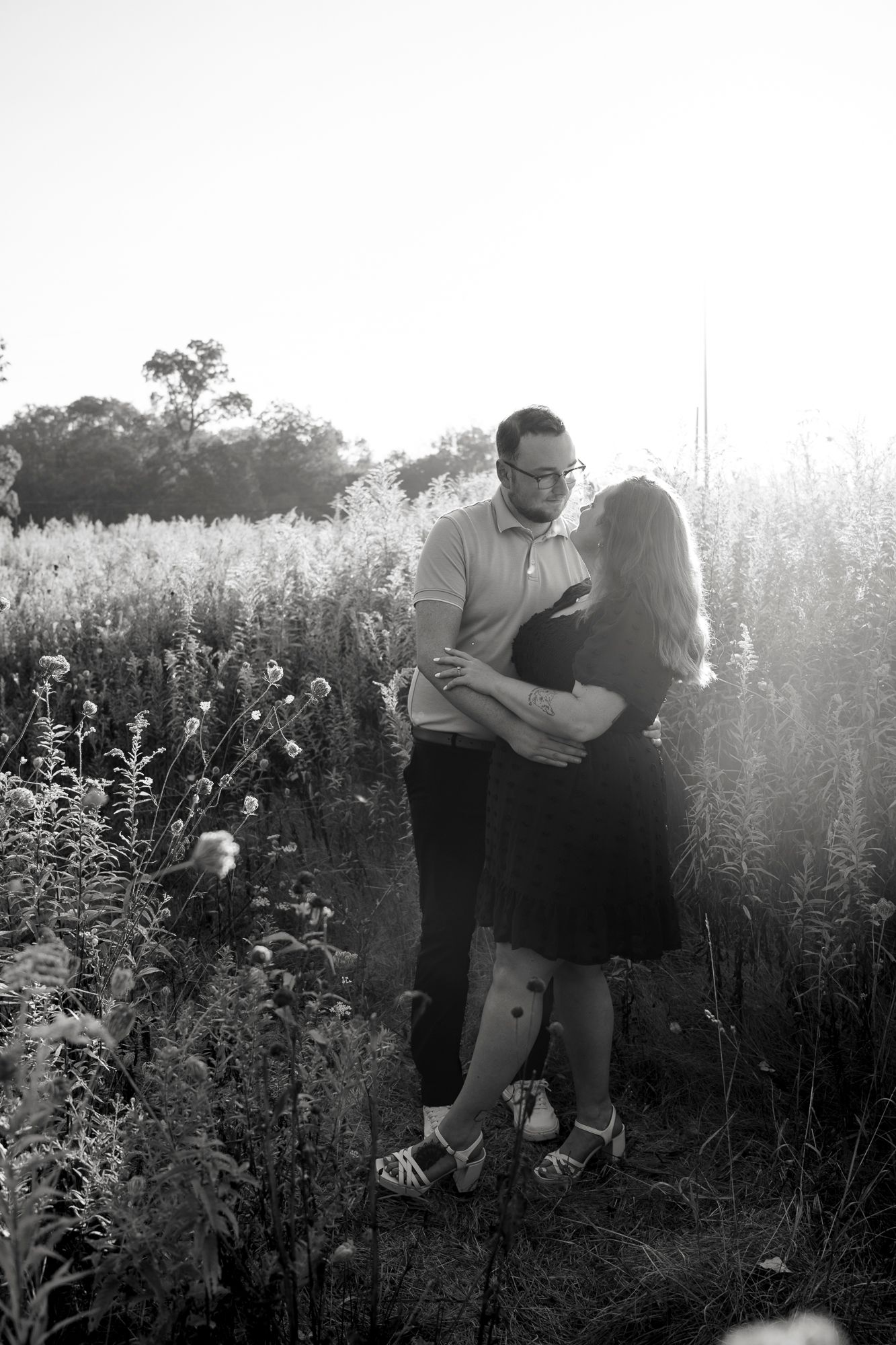 A couple shares an intimate moment together in a sunlit meadow filled with tall wildflowers and grasses.