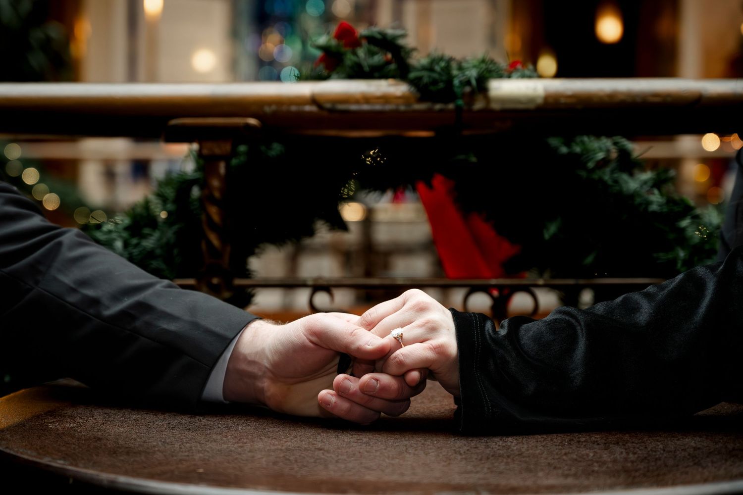 Two people holding hands across a table with a festive Christmas wreath in the background.