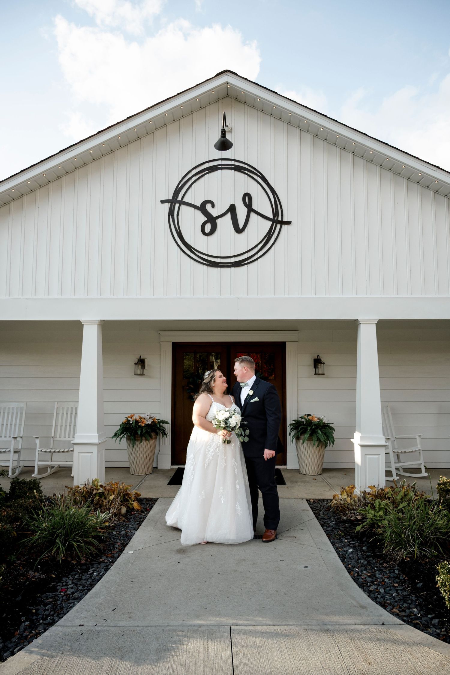 White wedding venue exterior with rocking chairs on the porch and a circular monogram sign above the entrance.