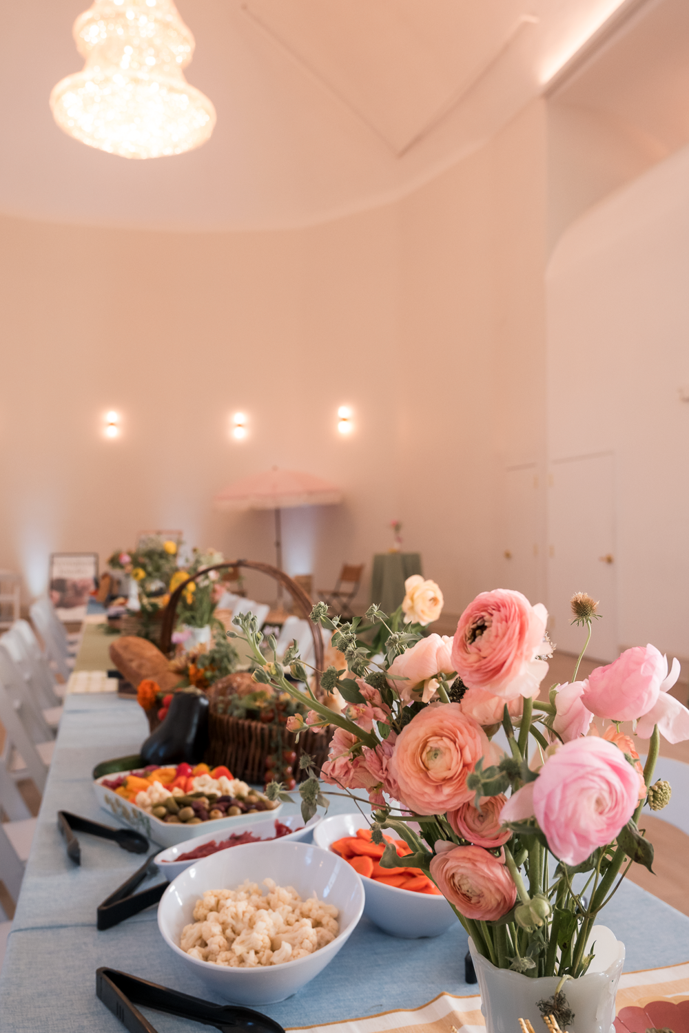 Elegant party table setting with pink ranunculus flowers and various appetizers served in white bowls.