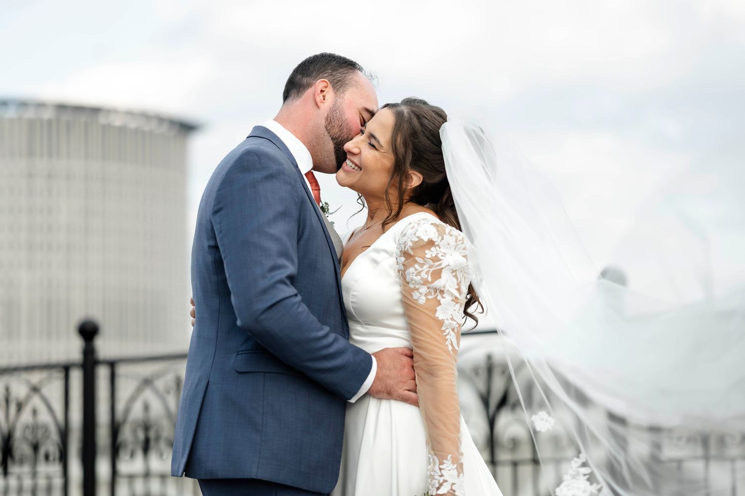 A romantic wedding couple embraces in front of a white building on their special day.