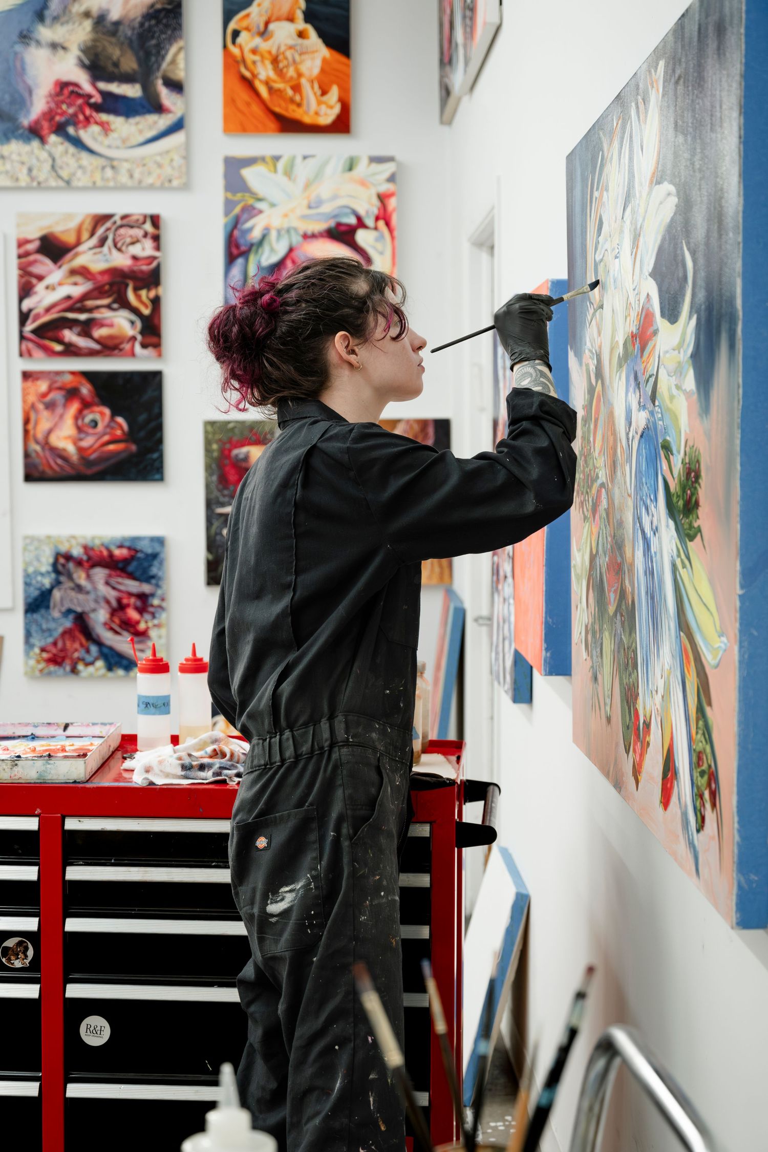 Artist working on colorful abstract artwork in gallery space with multiple paintings mounted on walls.