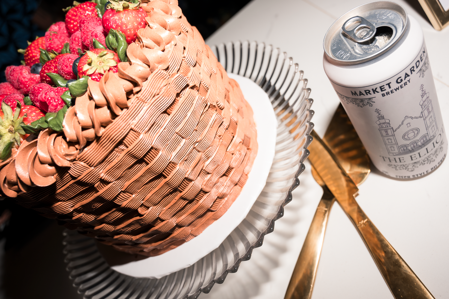 A pink frosted cupcake with silver sprinkles sits next to a silver beverage can on a white surface.