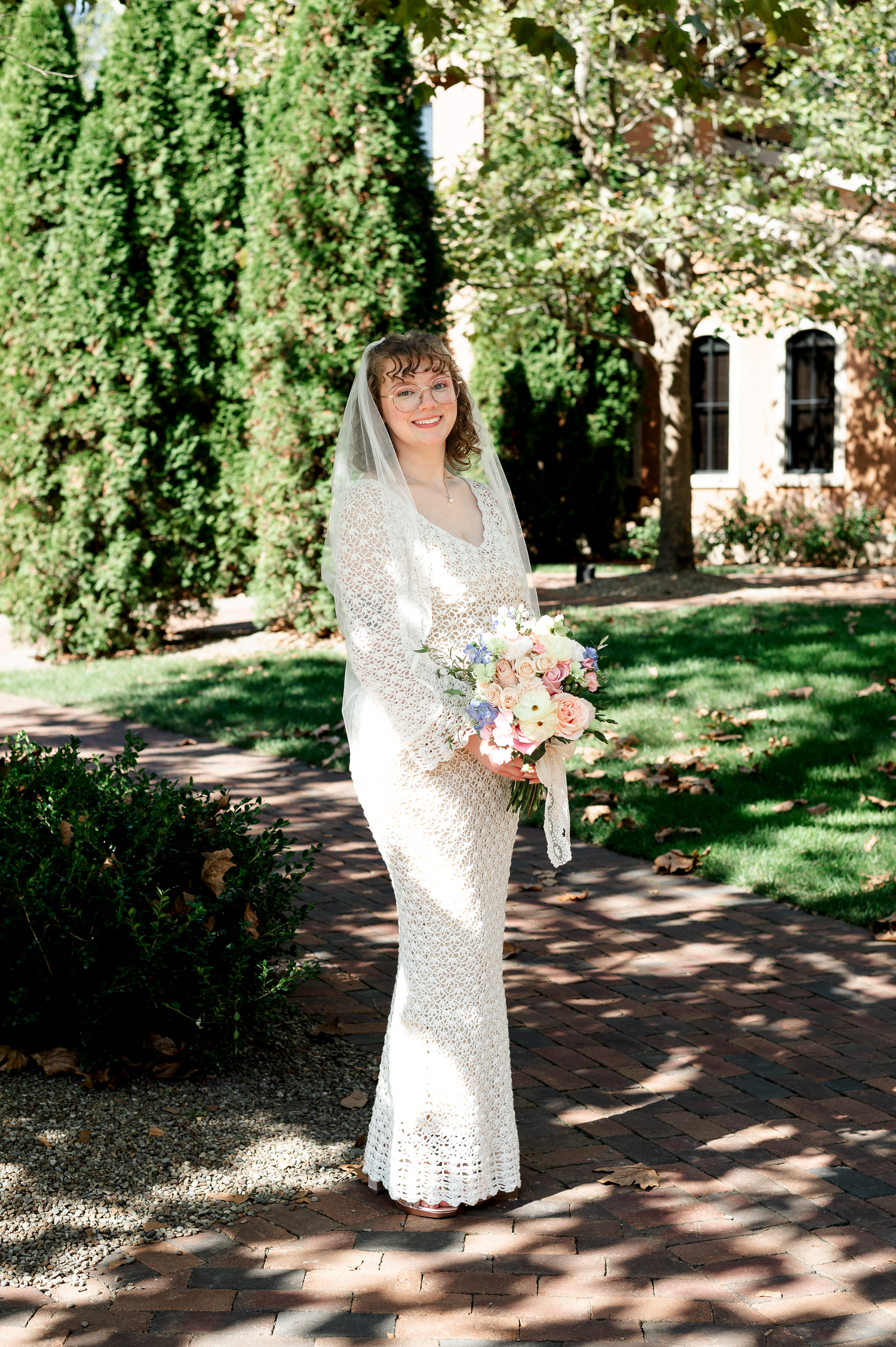 Bride in vintage-style lace dress holding colorful bouquet on garden path.