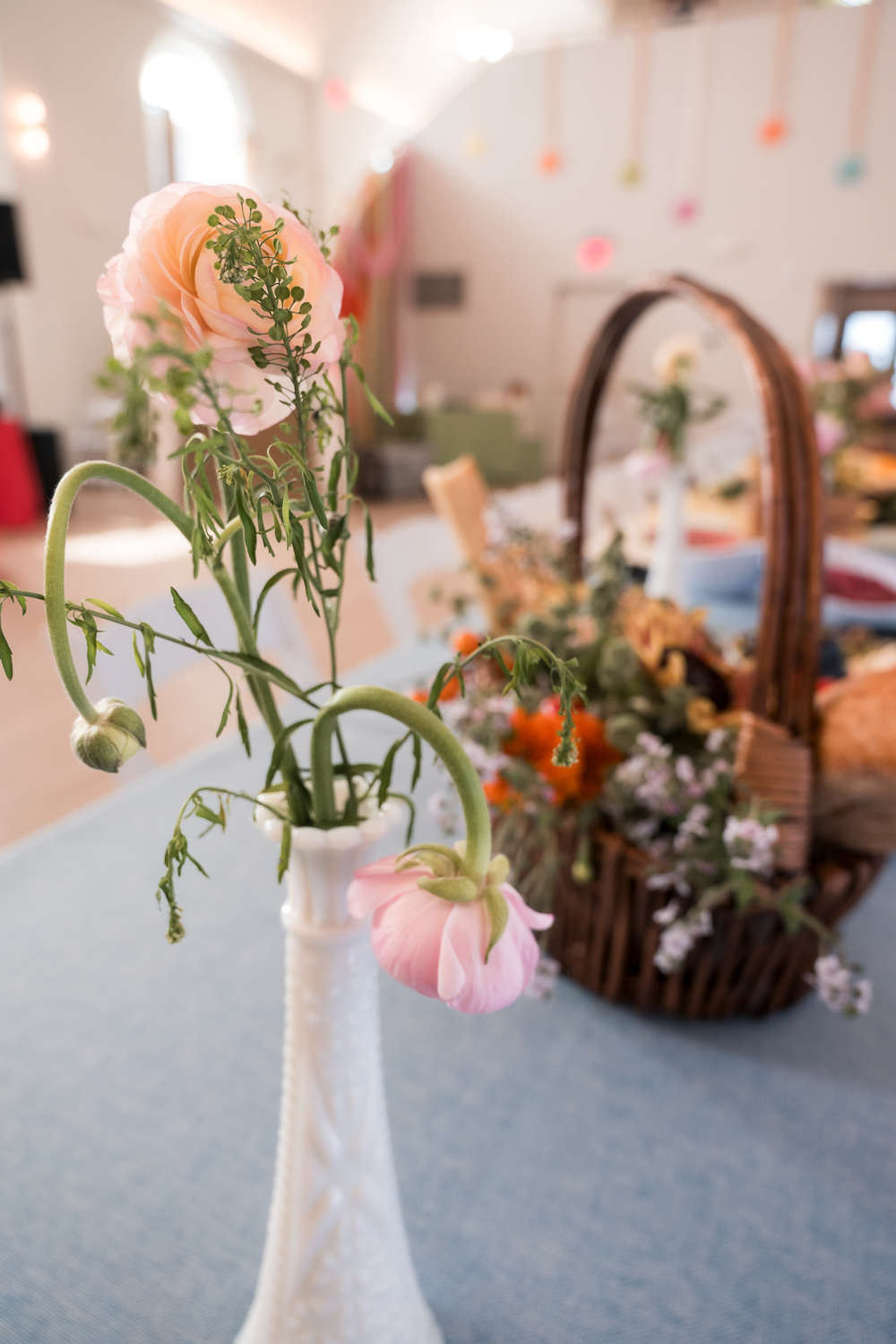 Delicate pink flowers and greenery arranged in white milk glass vases on a gray tablecloth for an elegant table setting.