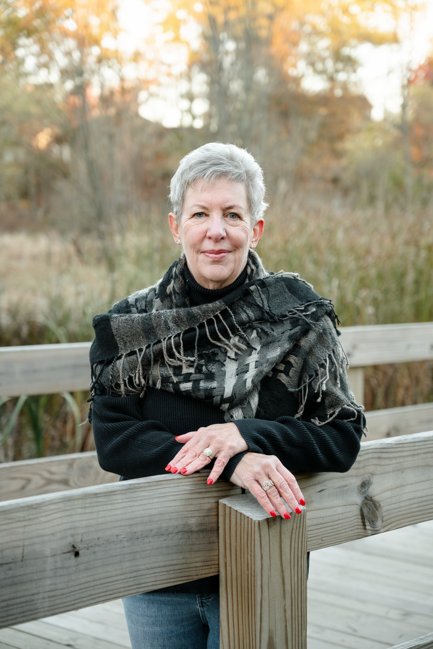 Person leaning on wooden railing wearing black jacket with fringe detail.