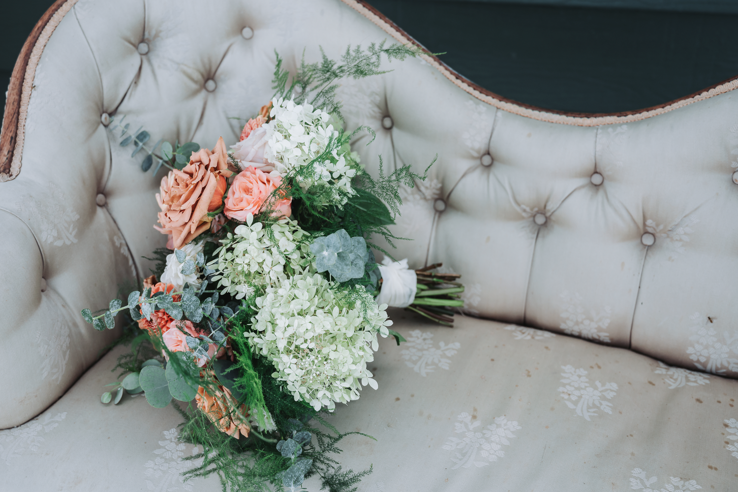 Elegant floral arrangements with coral roses displayed on a tufted white couch.