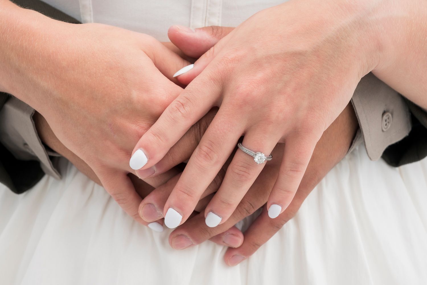 Close-up of bride and groom hands showing wedding ring and engagement ring with white manicured nails.