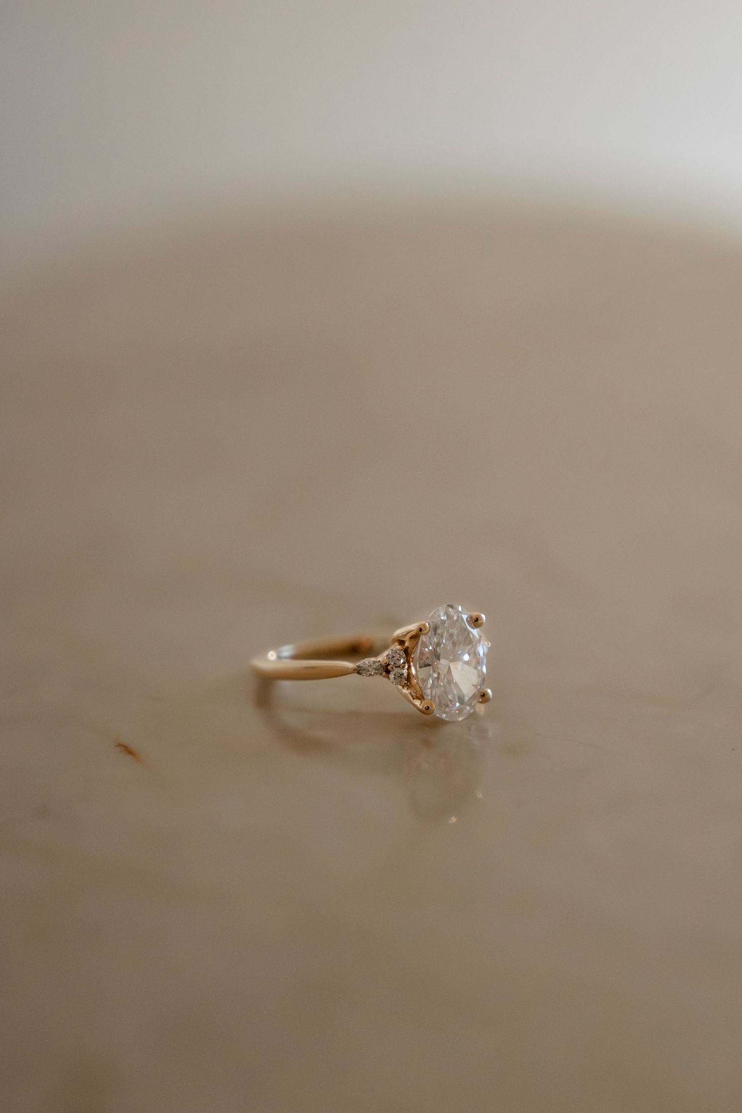 Gold engagement ring with large oval diamond solitaire on marble surface.