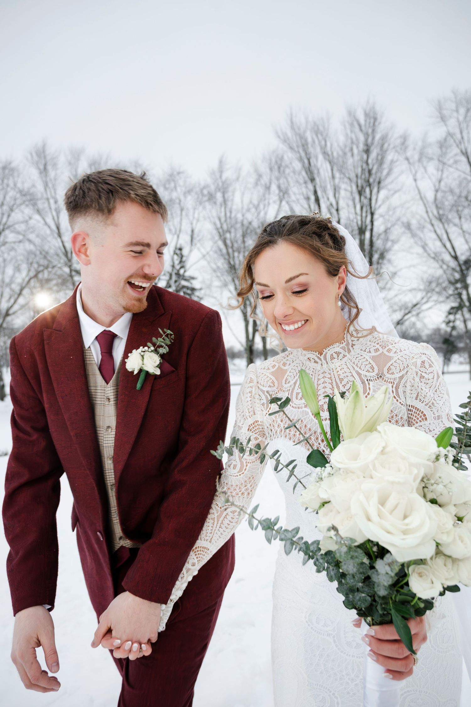 A bride and groom standing in the snow, the bride holding a bouquet of white flowers.