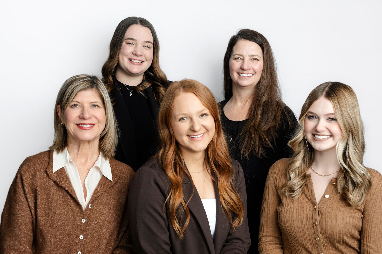 Professional headshots of team members wearing earth tone sweaters and blazers against a white background.