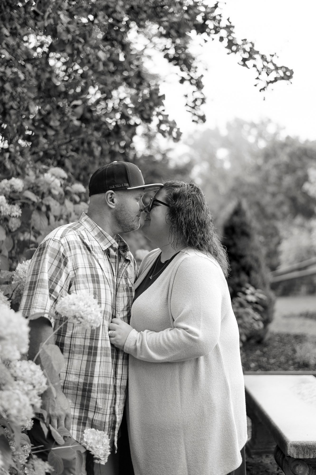 A romantic black and white photo series showing a couple in plaid and white embracing outdoors in a garden setting.